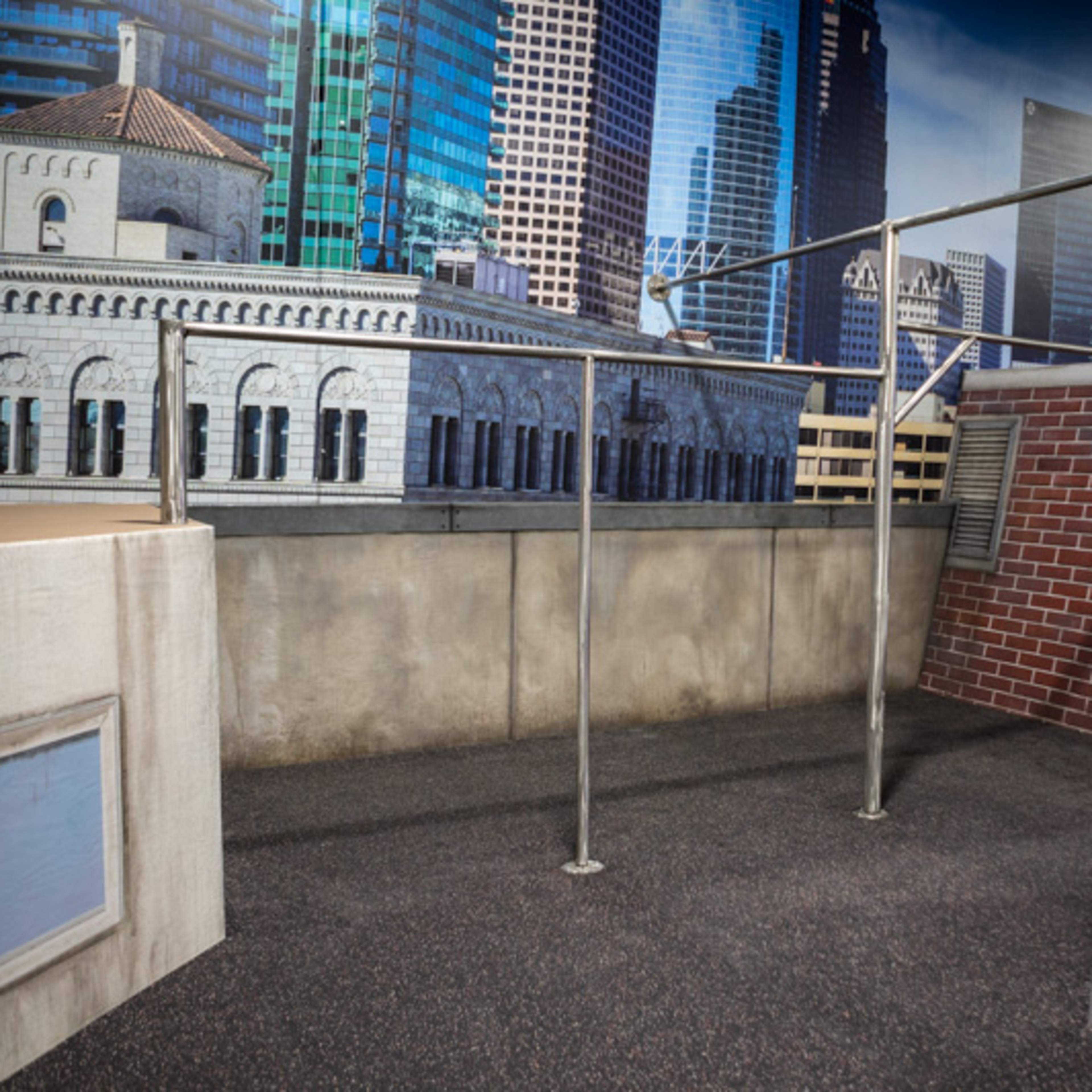 A rooftop setting with a metal framework and various urban architectural elements, including buildings and a skyline backdrop.