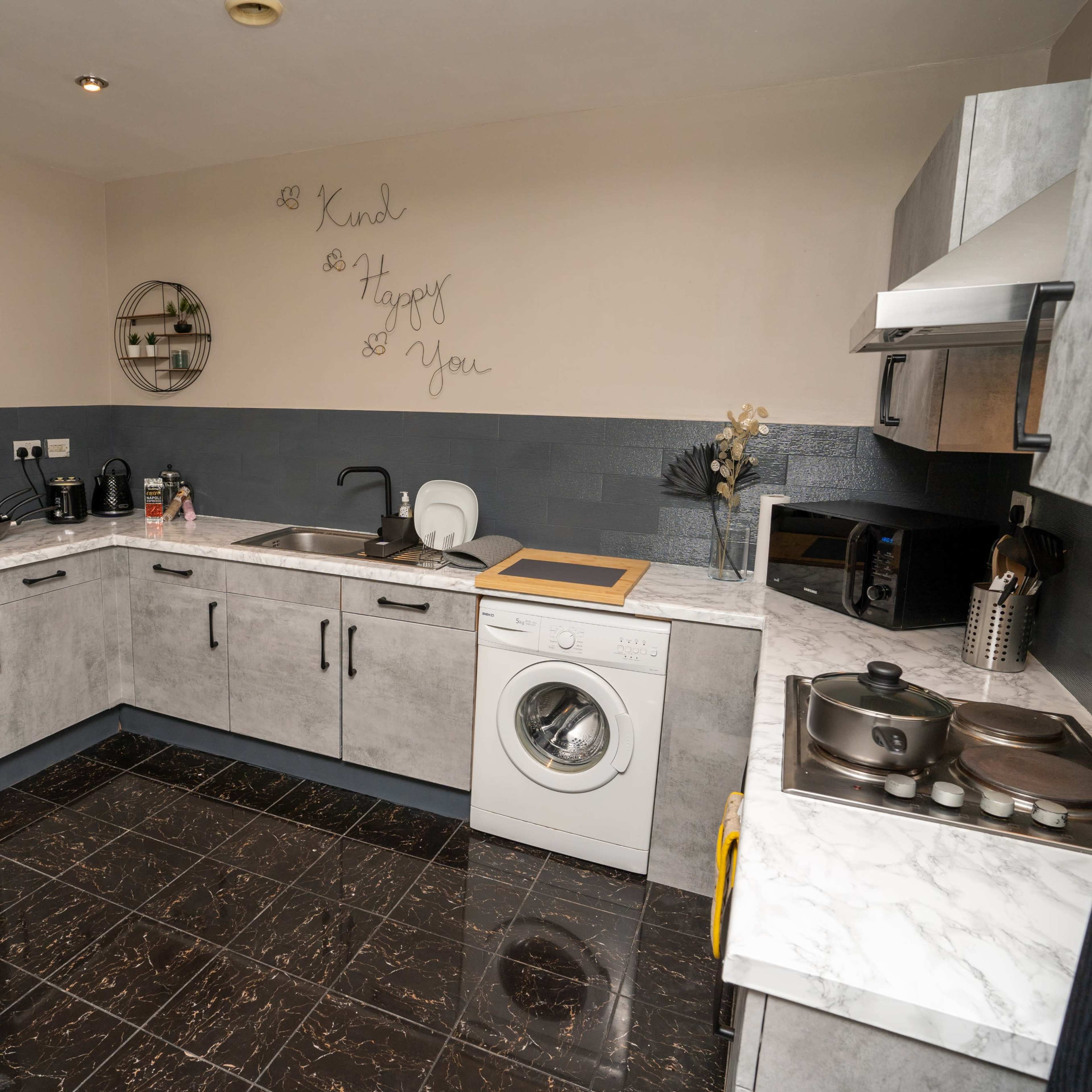 A modern kitchen with gray cabinets, stainless steel appliances, a washing machine, and a marble countertop.