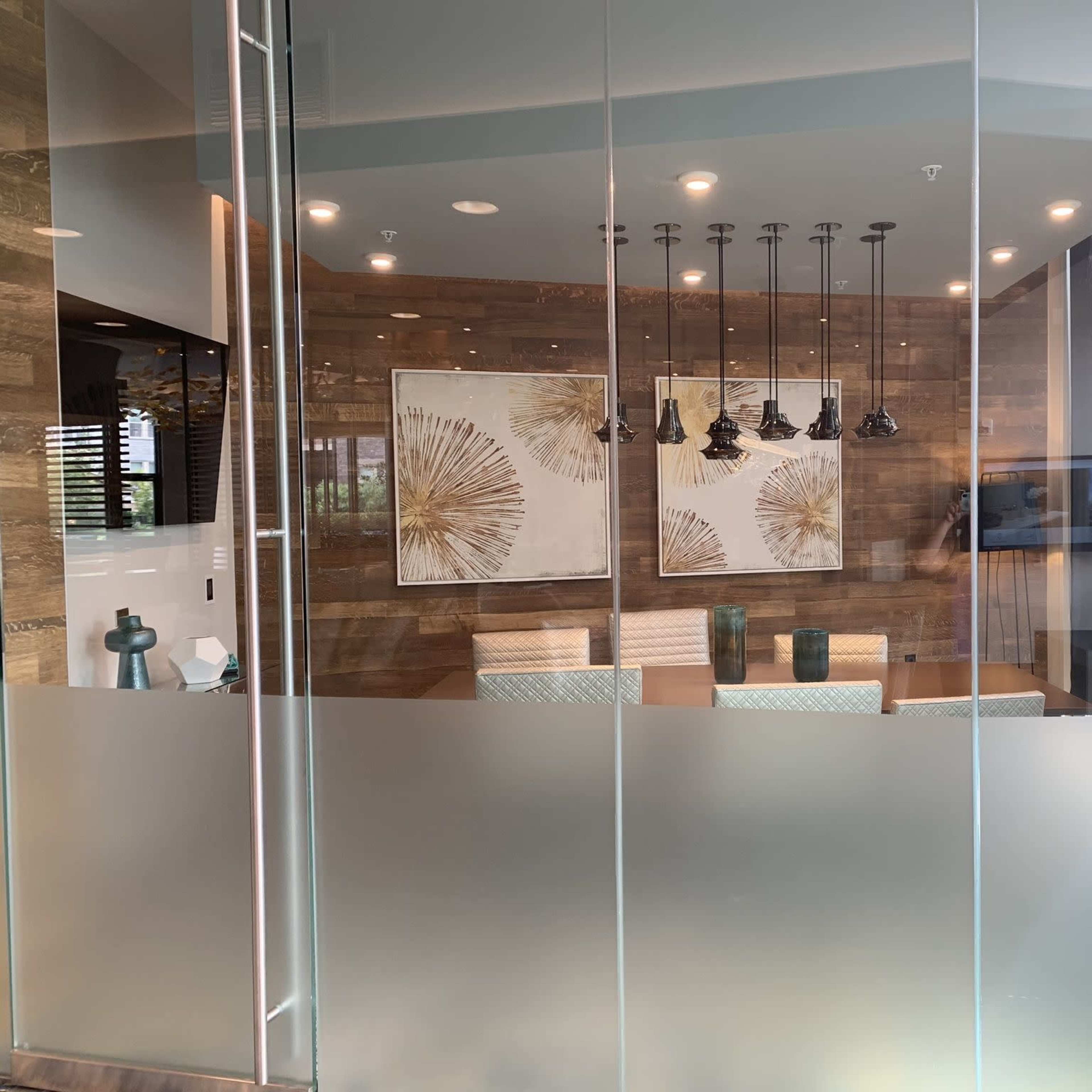 A modern office space with frosted glass walls, featuring a seating area, decorative art on the walls, and pendant lighting.