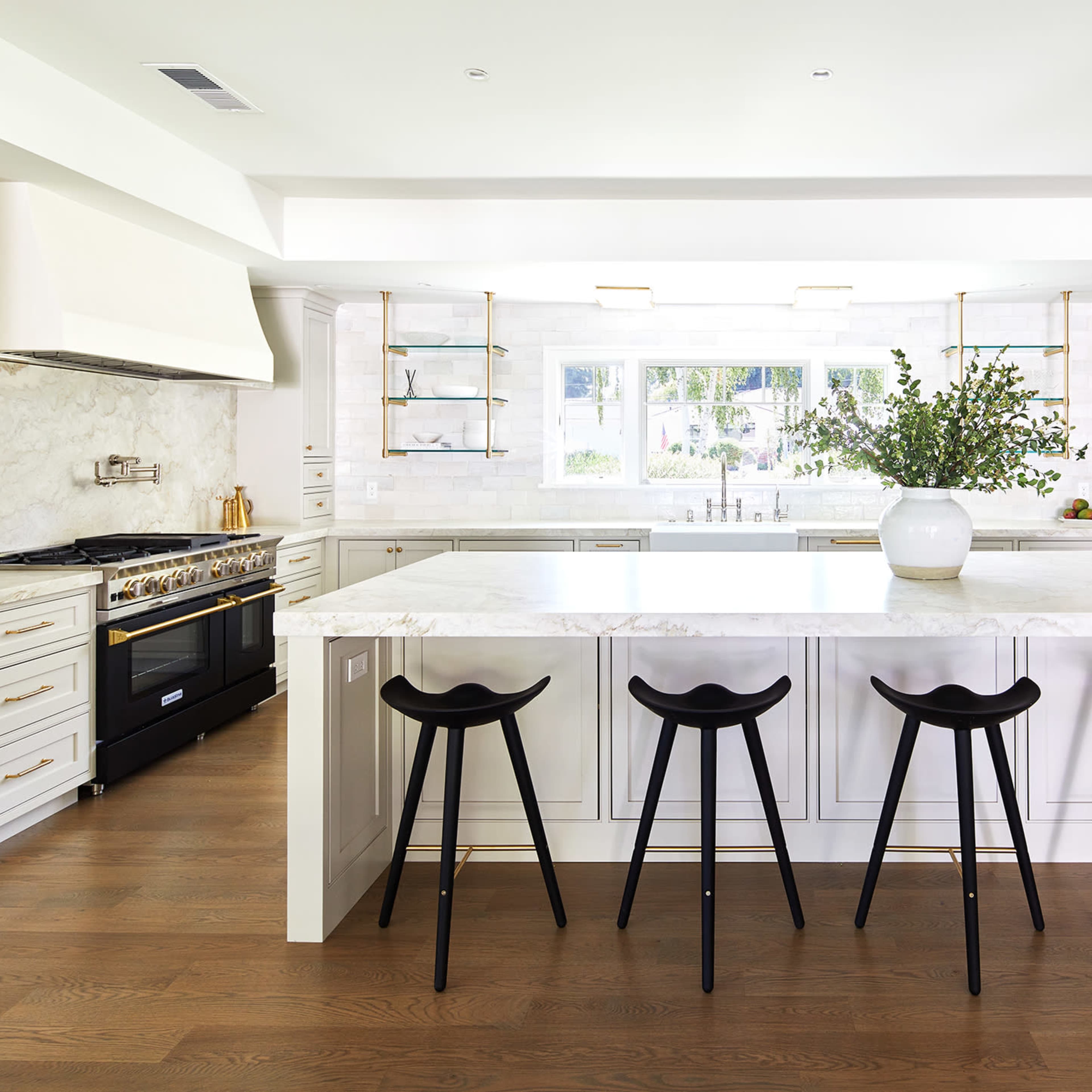 A spacious kitchen features a large marble island with black stools and modern cabinetry.