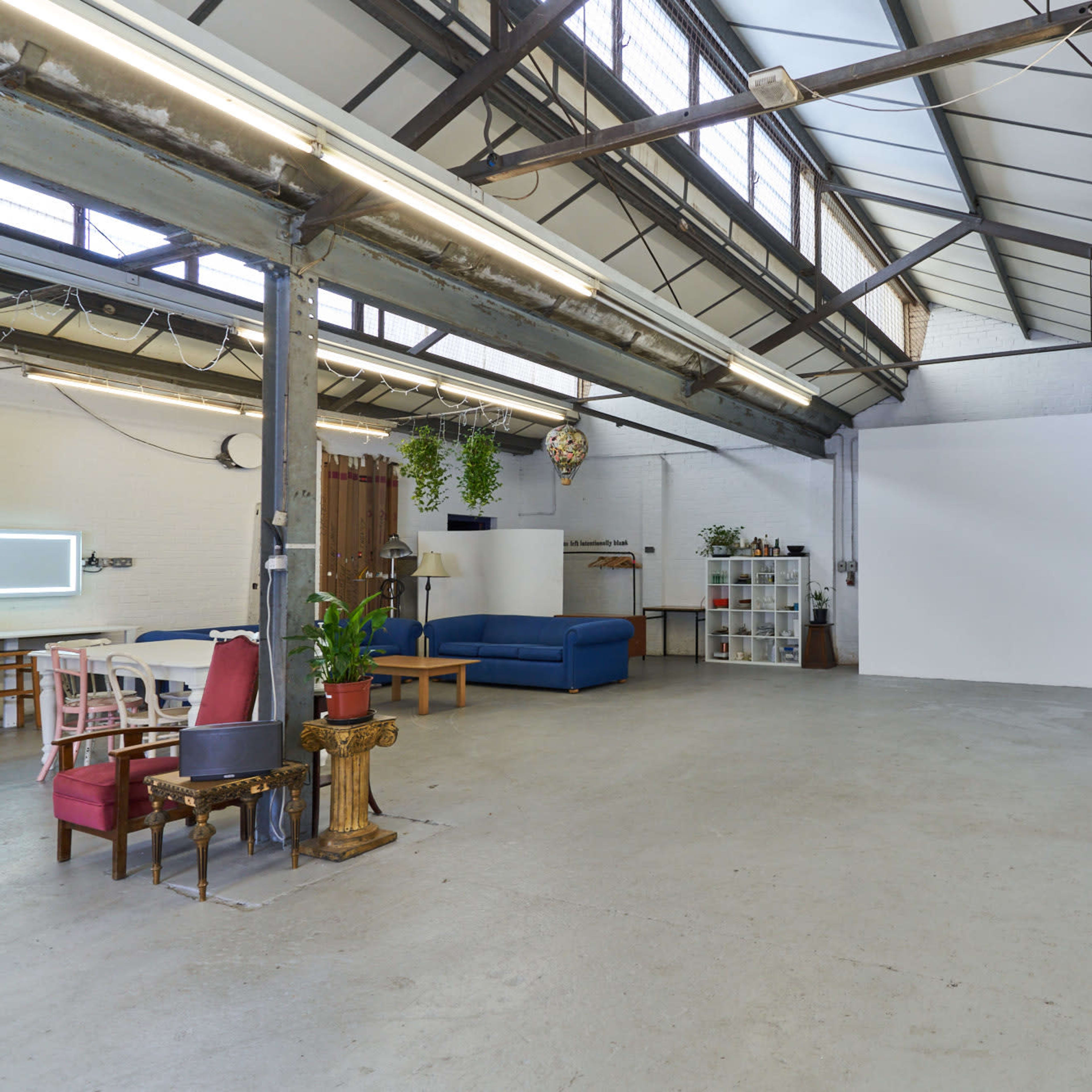 A spacious industrial-style room with high ceilings, a white wall, various seating areas, and shelves.