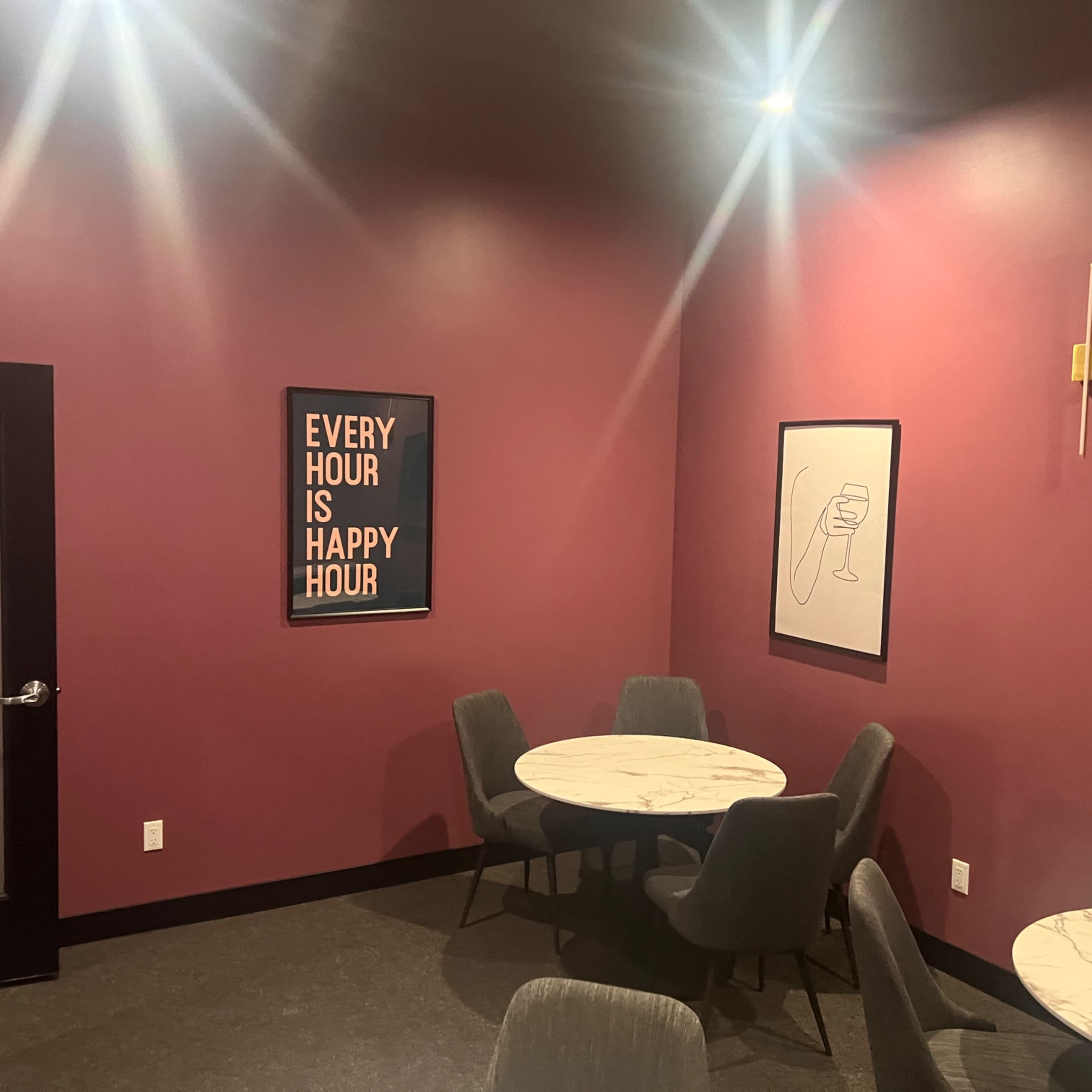 A dimly lit room with maroon walls, featuring marble-topped tables and a few chairs, along with framed artwork on the walls.
