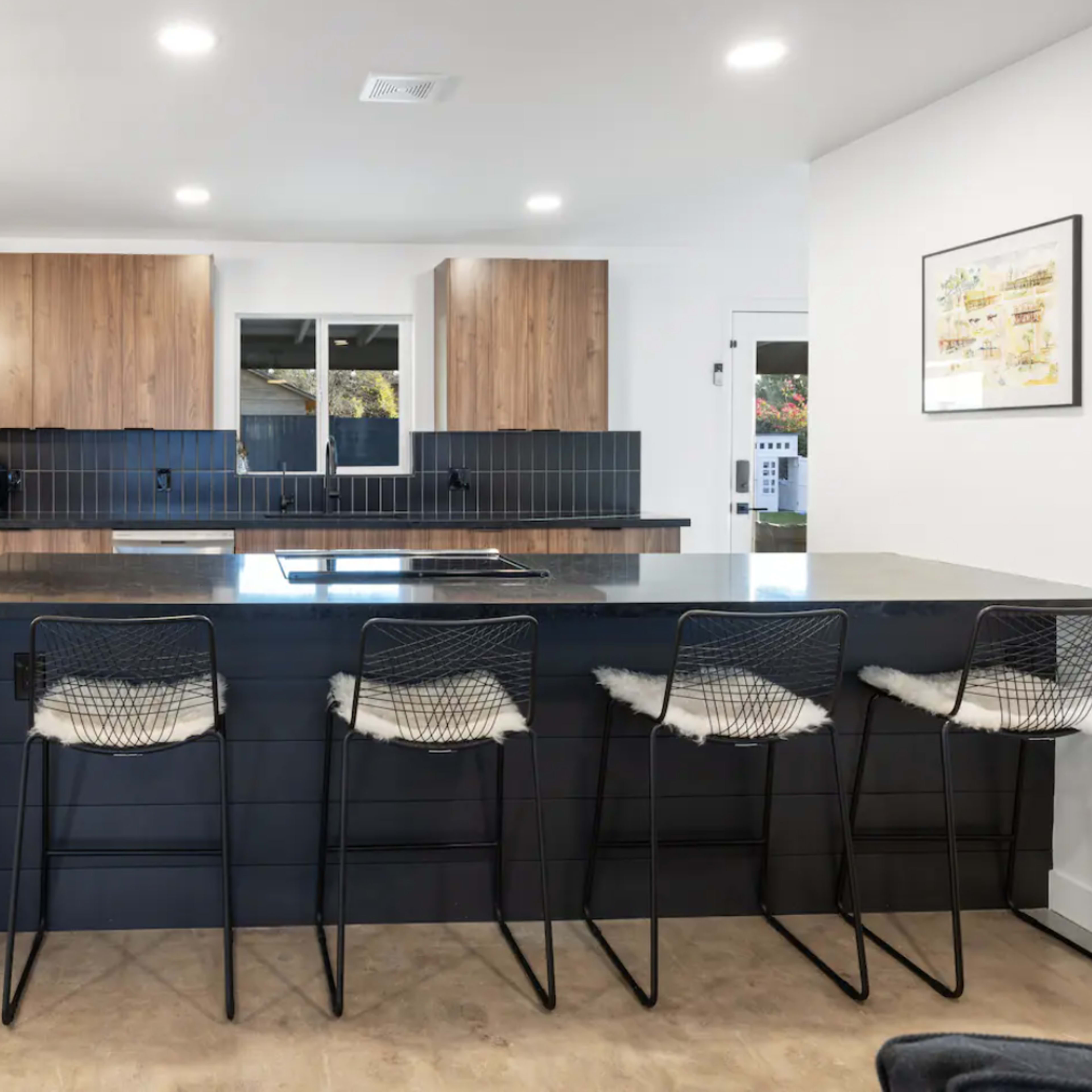 A modern kitchen featuring wooden cabinetry, stainless steel appliances, and a black countertop with bar stools.