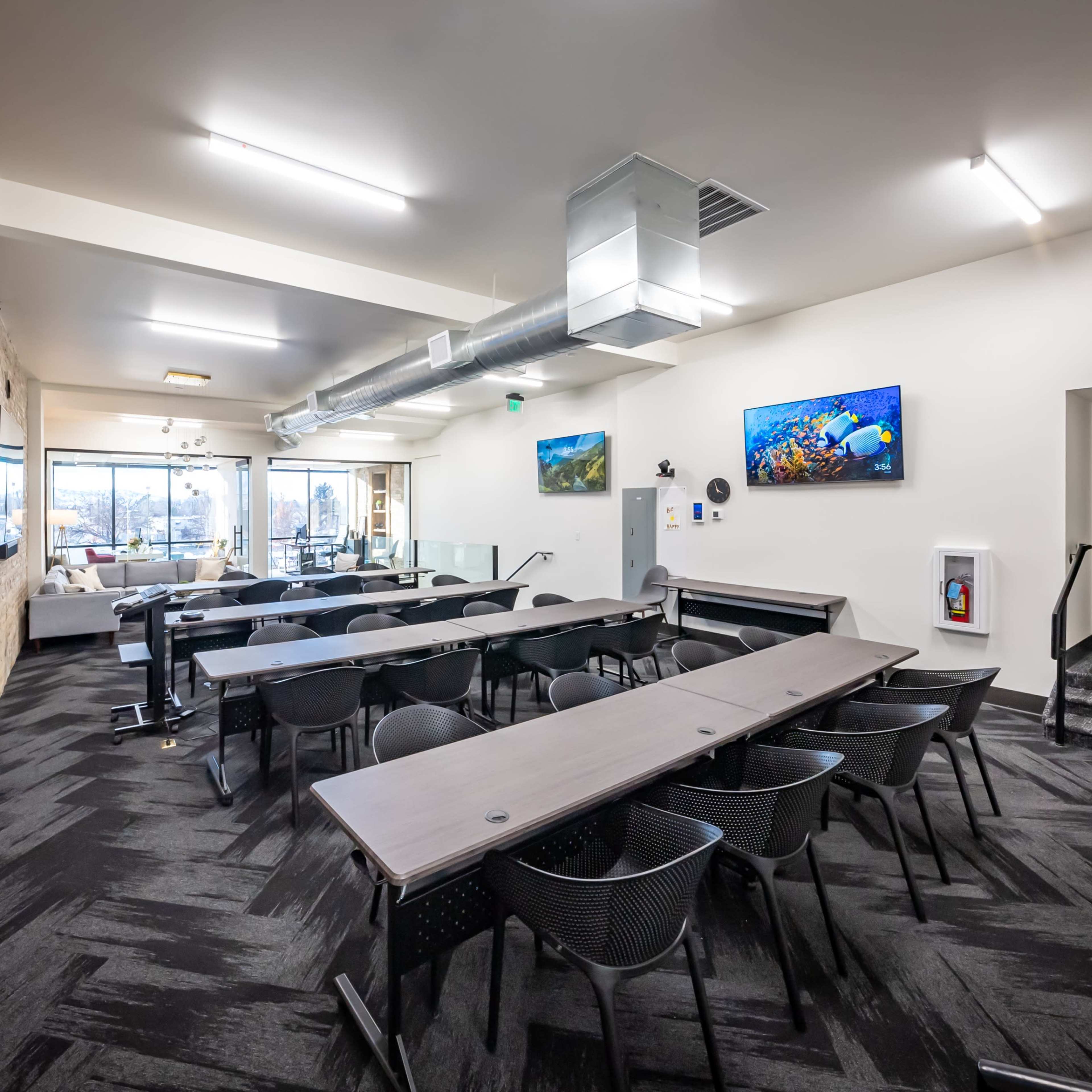 A modern conference room with several tables and chairs arranged for meetings, featuring large windows and wall-mounted screens displaying underwater scenes.