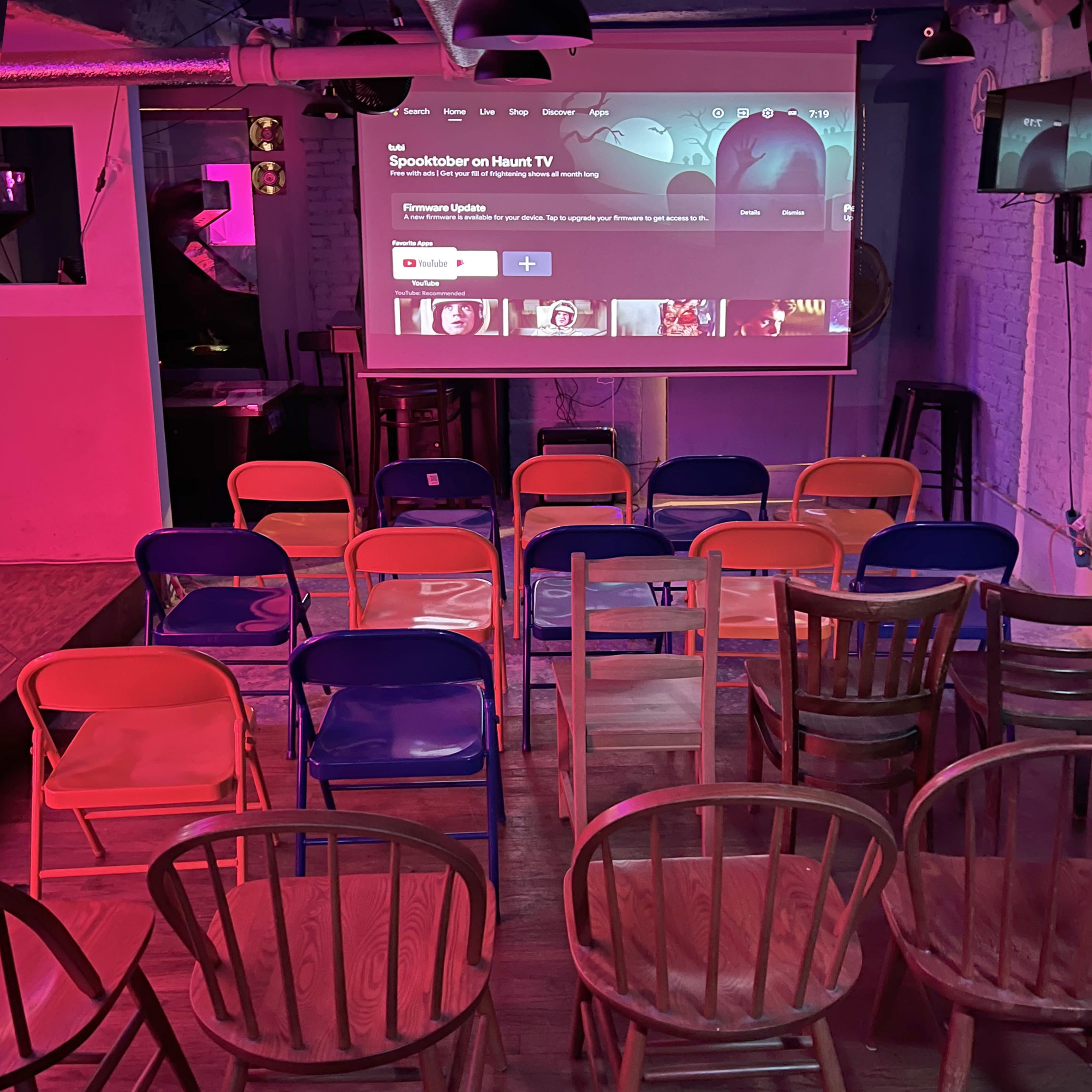 A room set up for an event, with an array of colorful chairs facing a projection screen displaying a YouTube interface.
