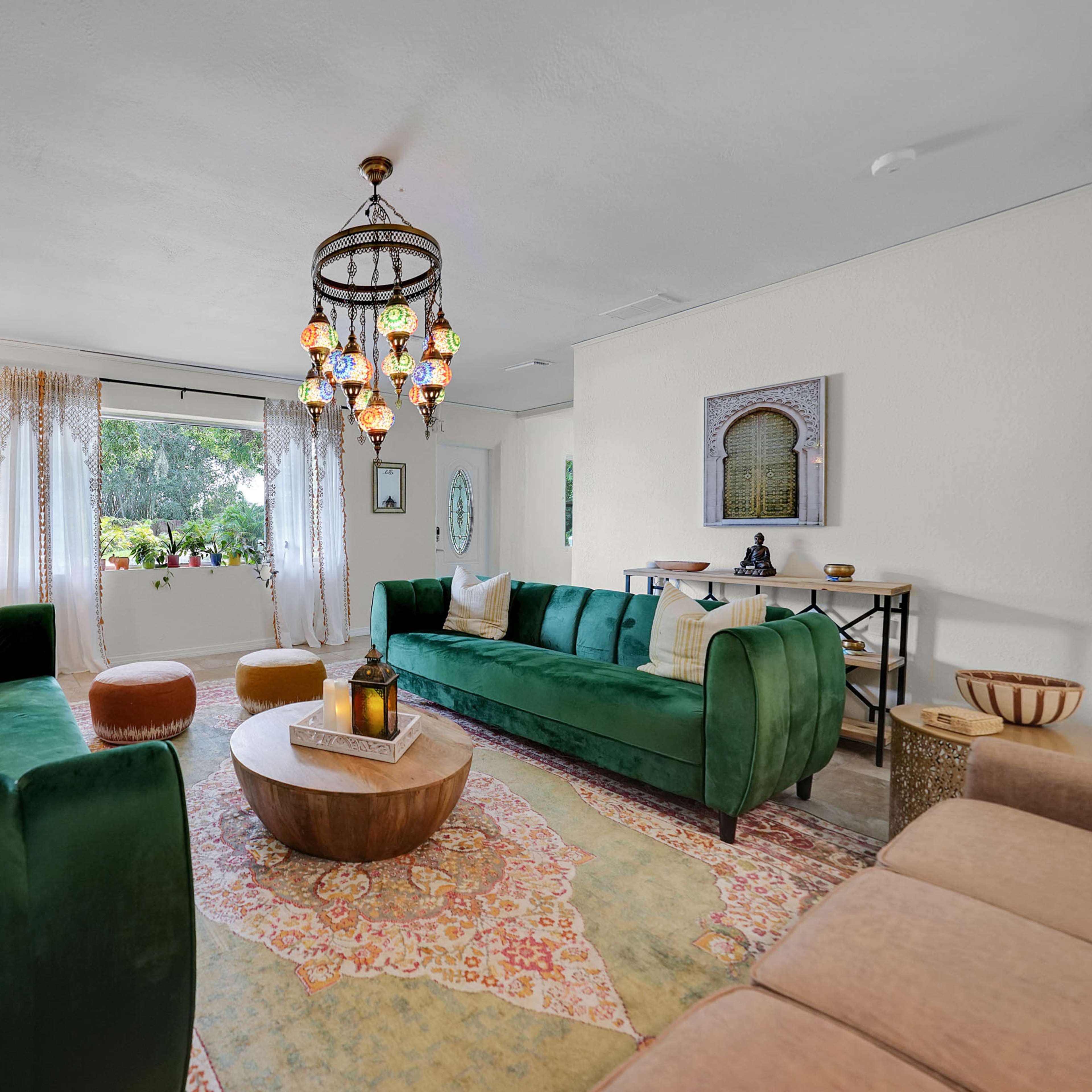 A spacious living room features two green sofas, a round wooden coffee table, and a decorative chandelier hanging overhead.