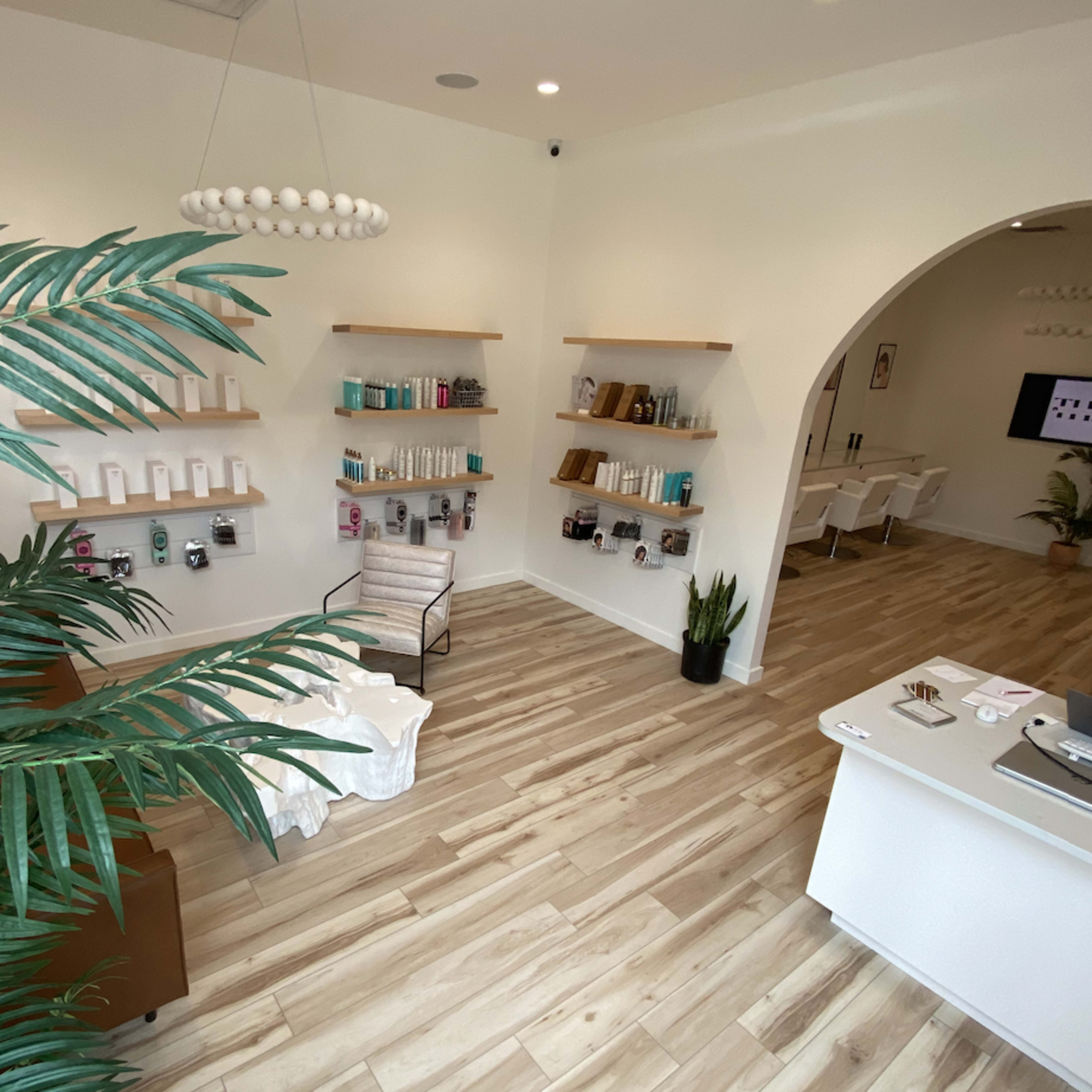 A modern interior of a spa-like space featuring wooden flooring, shelves displaying various products, and seating arrangements under a circular light fixture.