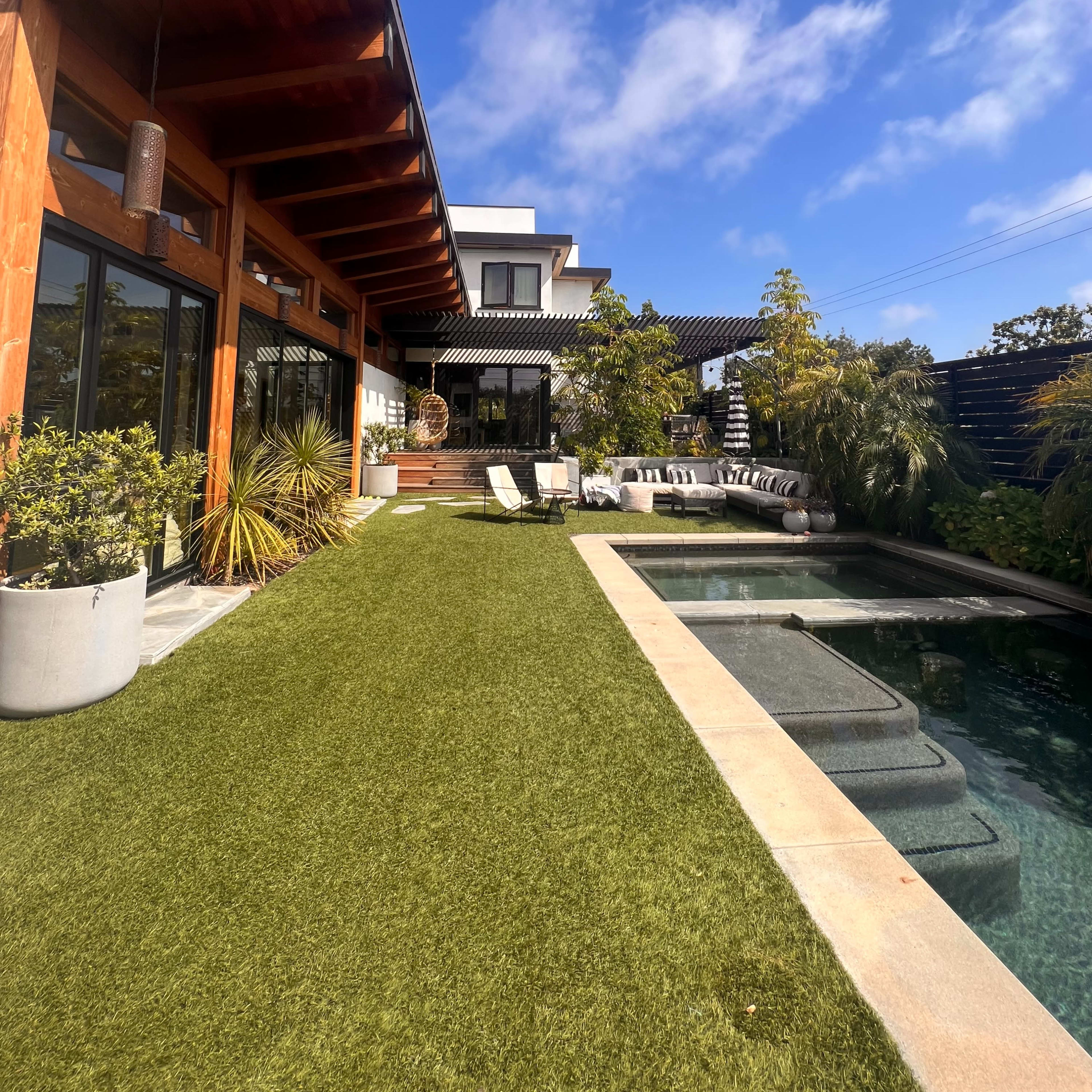 A modern home features a spacious lawn, a swimming pool, and a patio area with lounge chairs under a clear blue sky.
