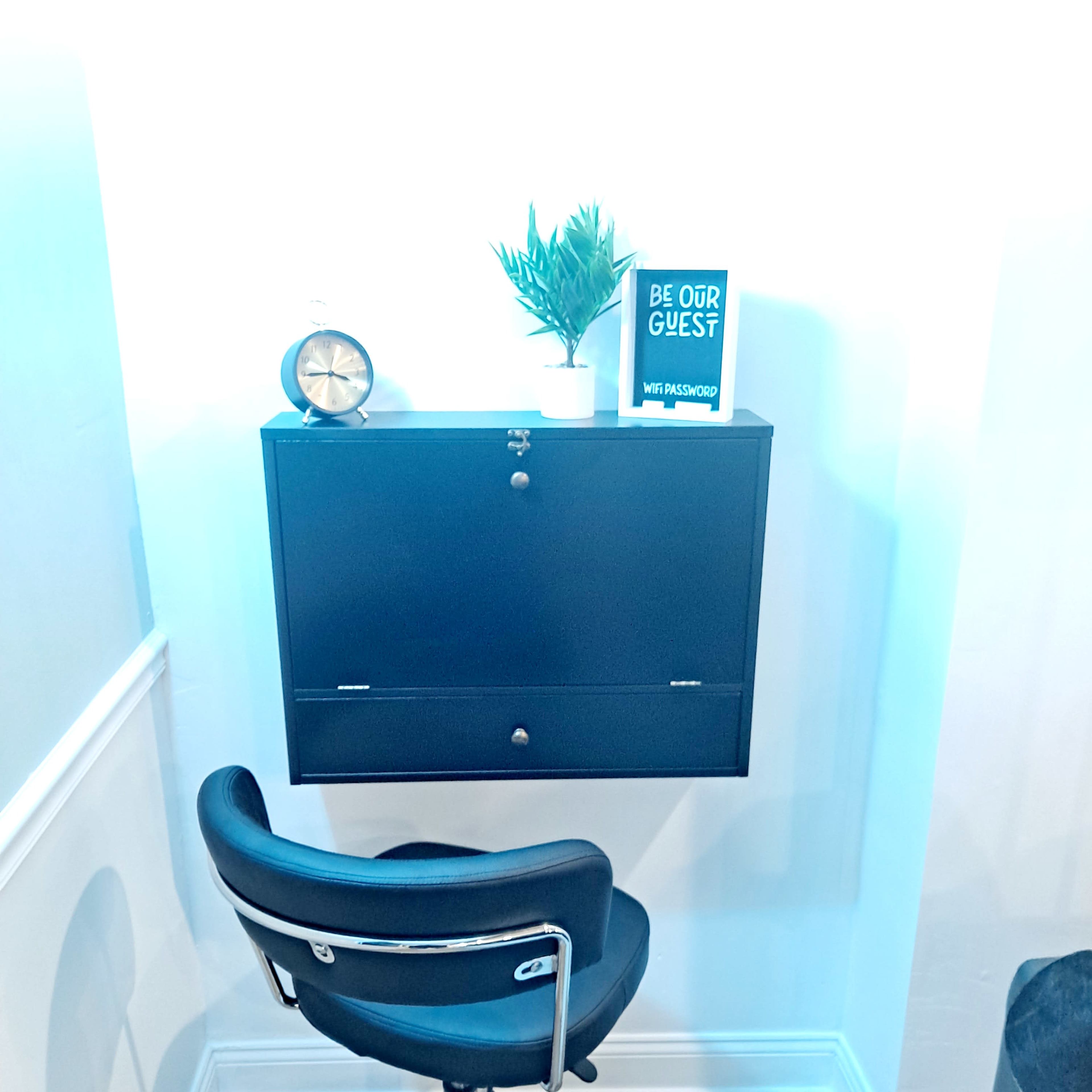 A black wall-mounted cabinet with a potted plant and a clock is placed beside a swivel chair on a wooden floor.