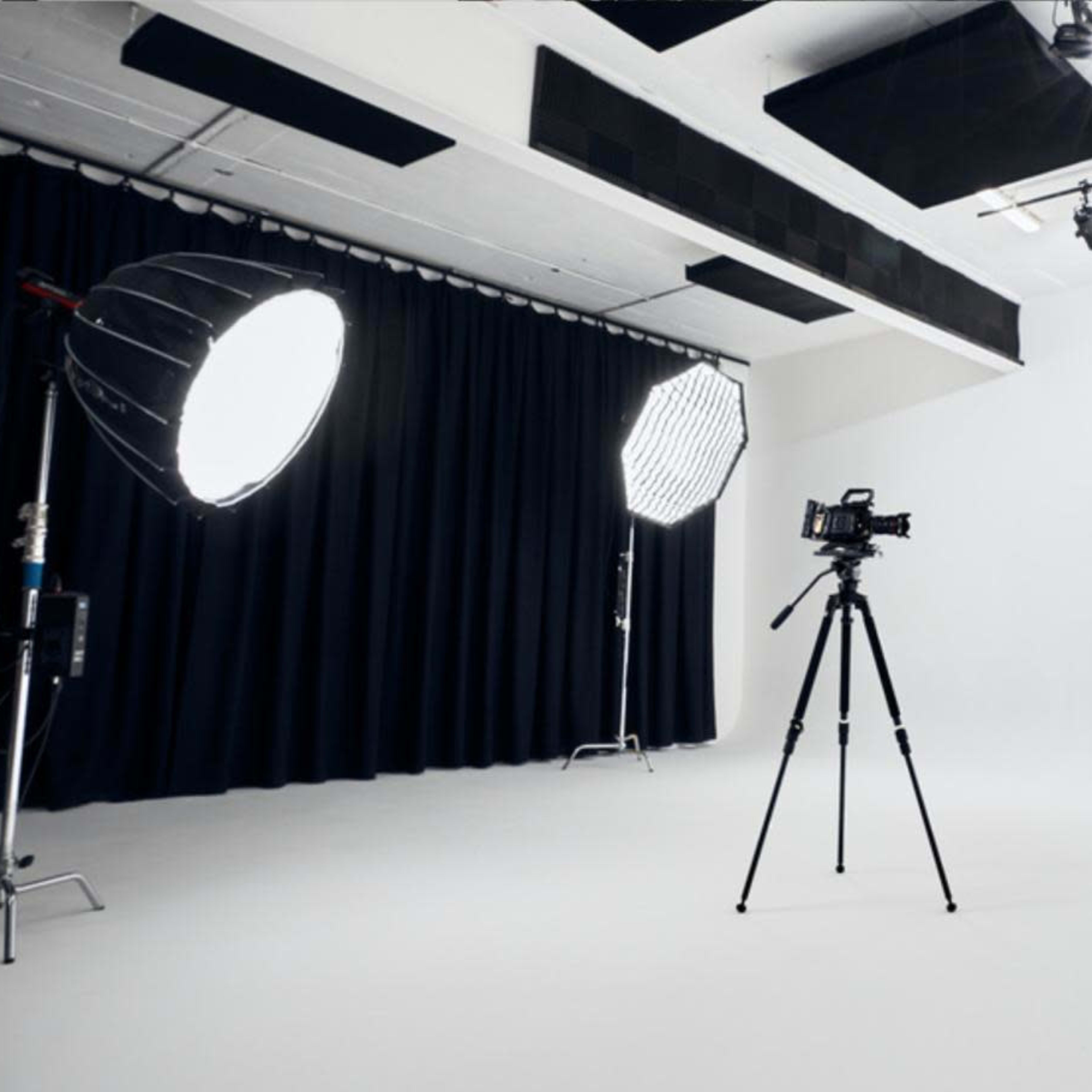 A photography studio equipped with lighting setups, a camera on a tripod, and a microphone on a stand against a plain white background.