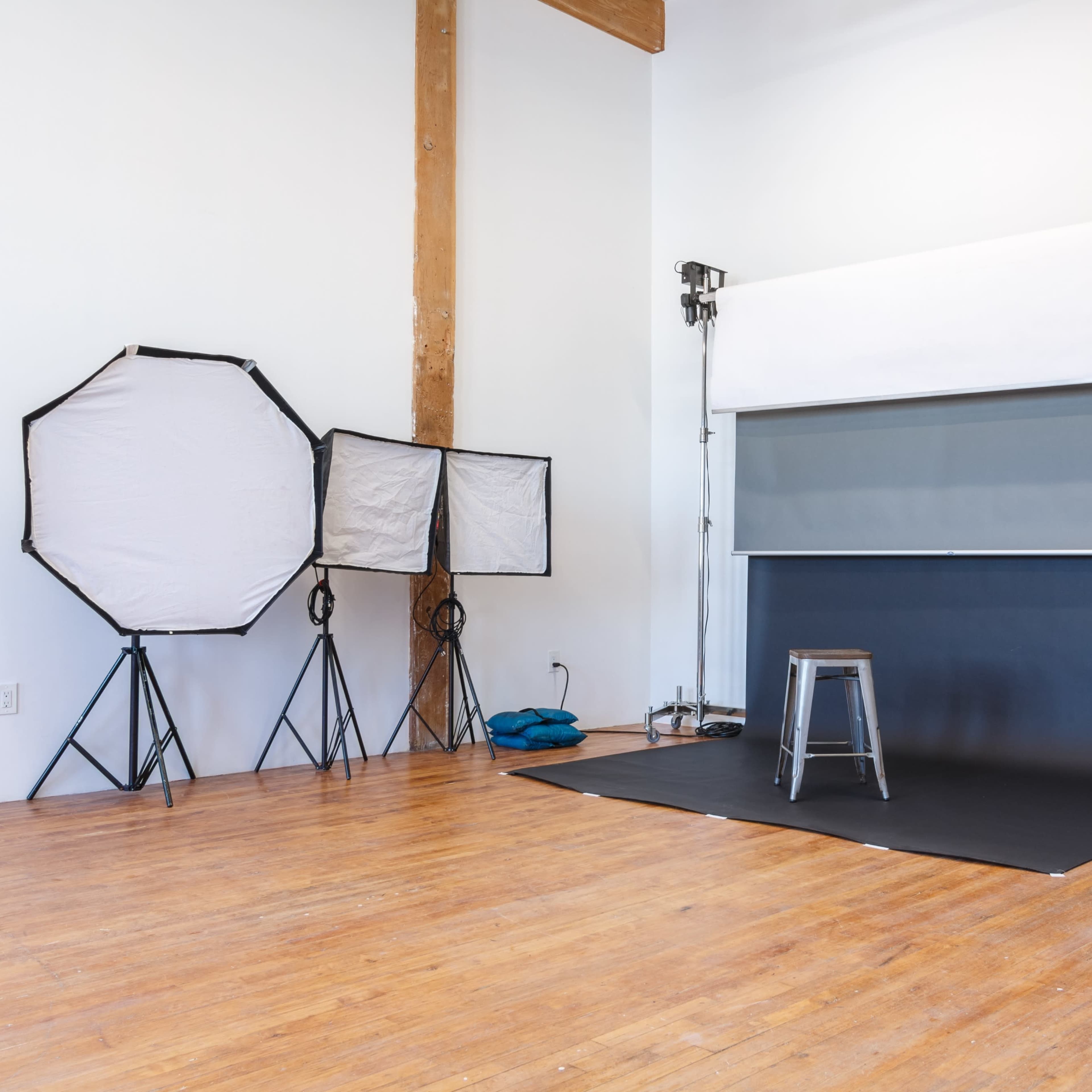 A photography studio with two softboxes, a grey backdrop, a metal stool, and wooden flooring.