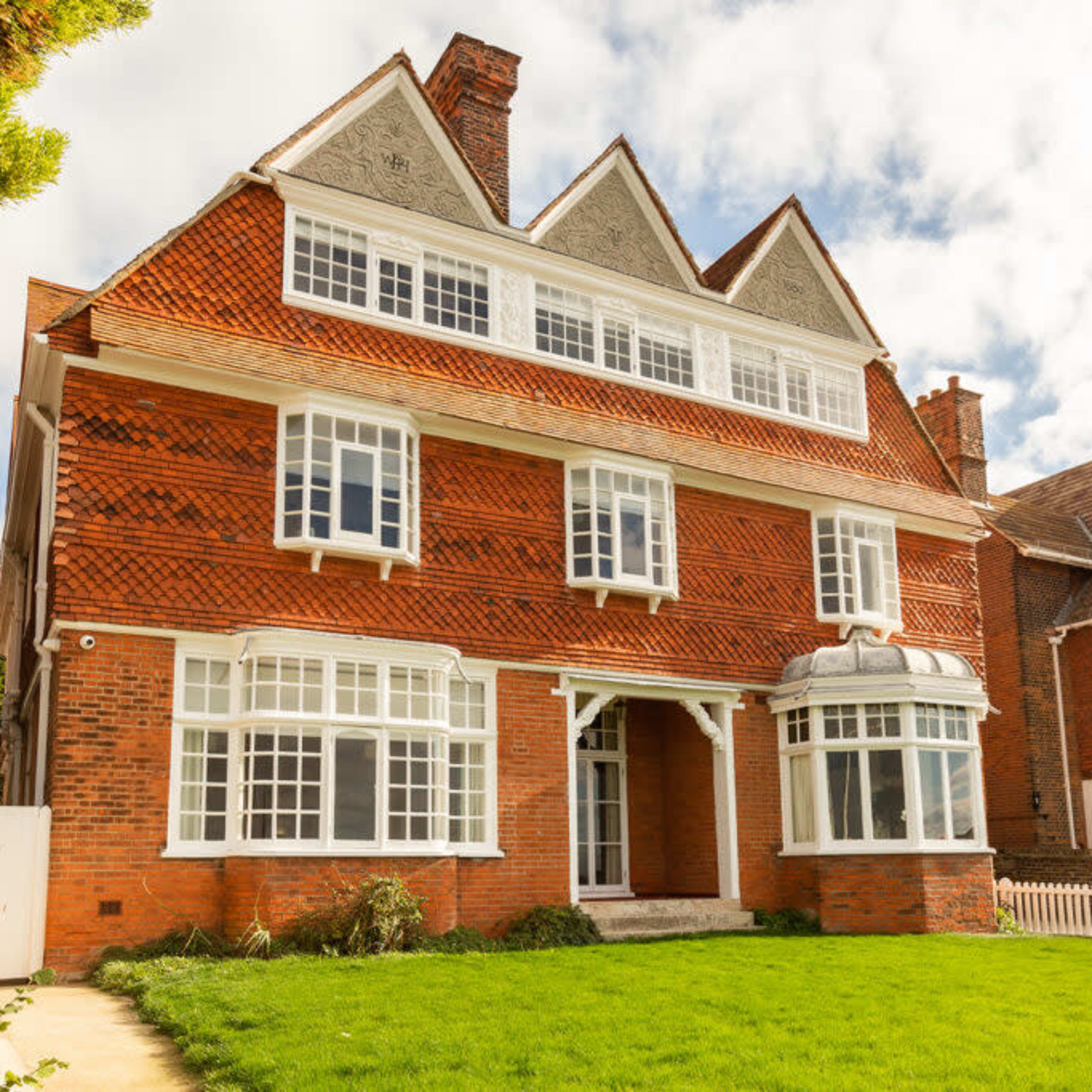 A large, three-story red brick house with multiple gabled roofs and a front lawn.