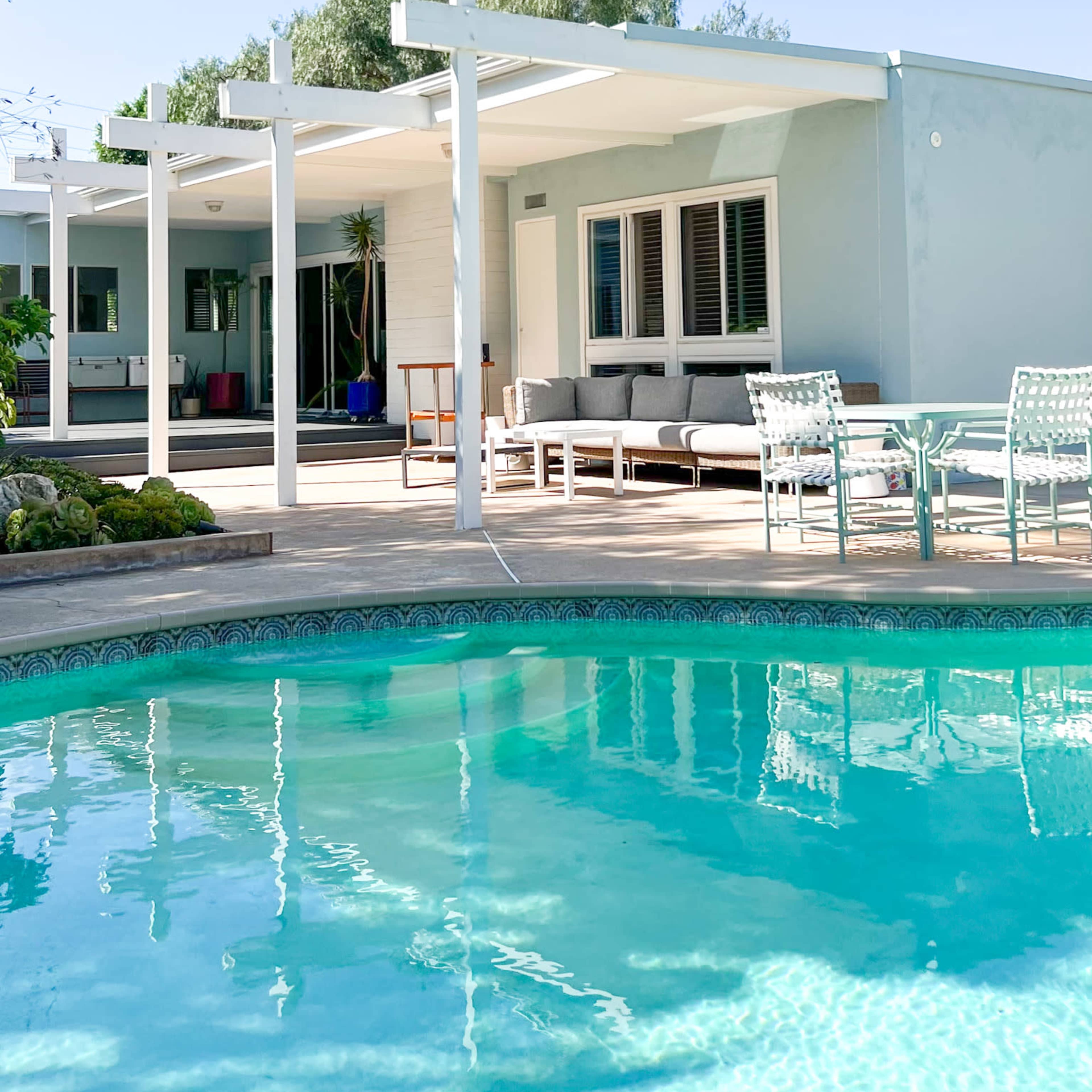 A modern home with a swimming pool in the foreground and a patio area furnished with outdoor seating.