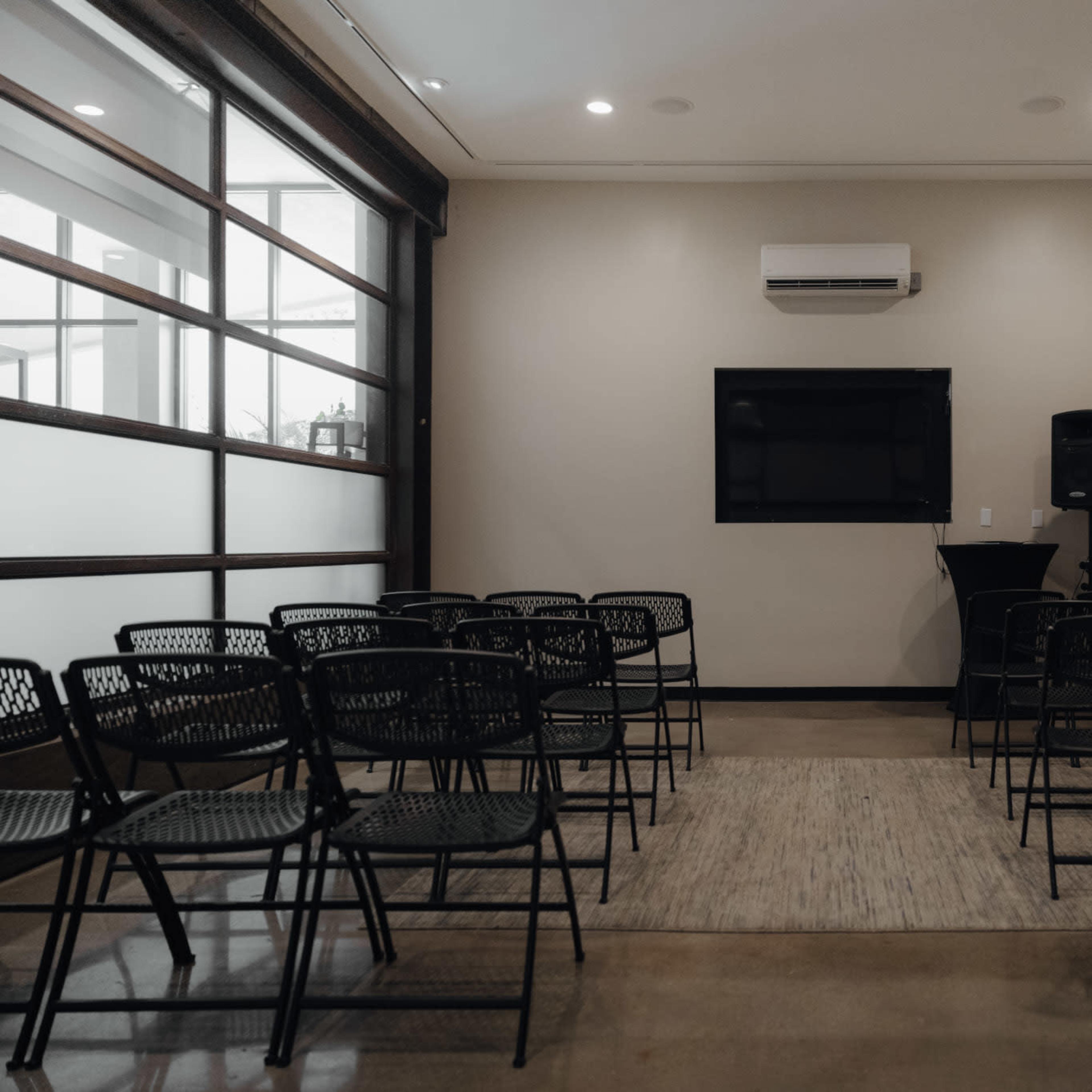 A meeting room is set up with rows of black chairs facing a wall-mounted TV and a speaker.