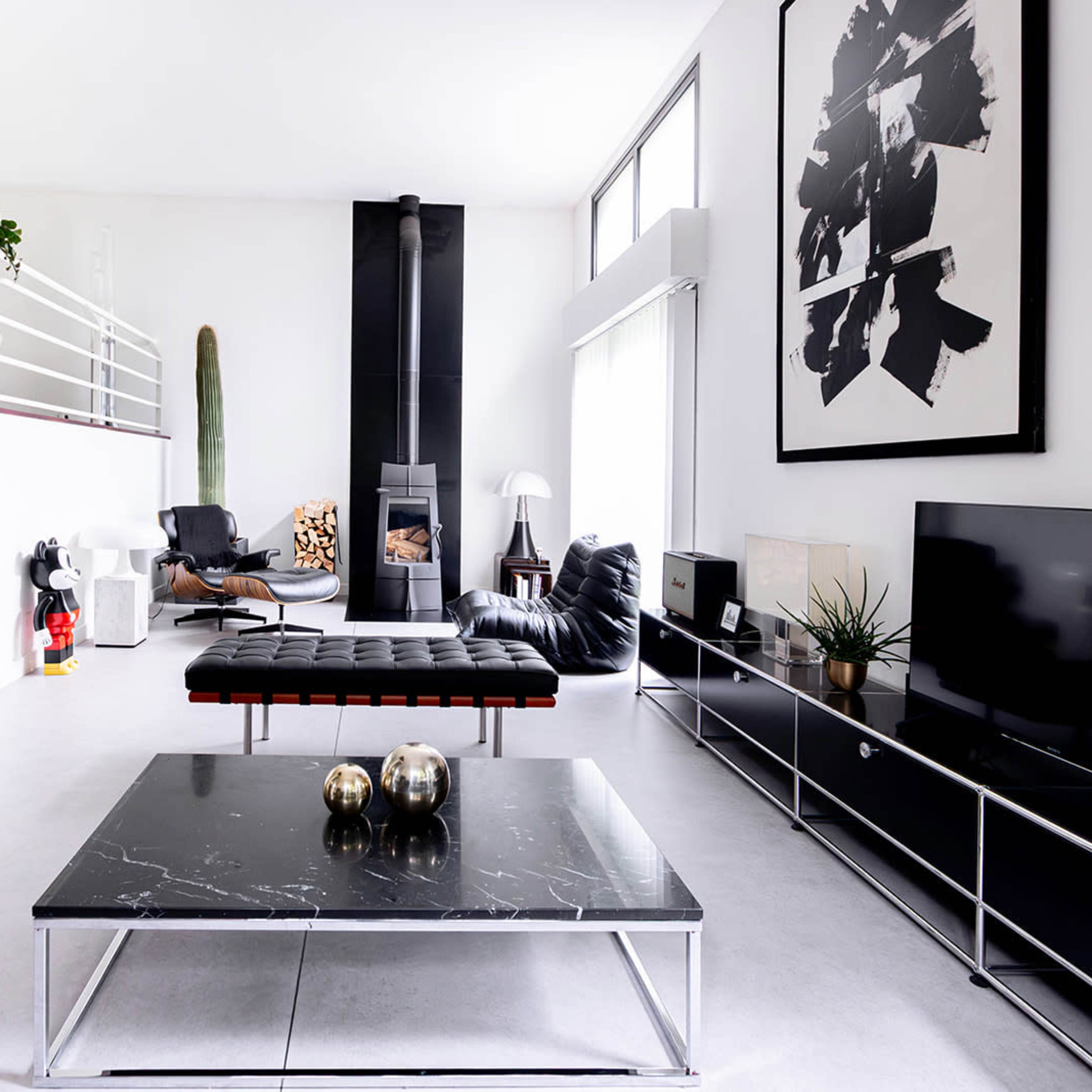 A modern living room featuring a large black coffee table, a sleek television stand, and a minimalist fireplace, with stylish furniture and indoor plants.