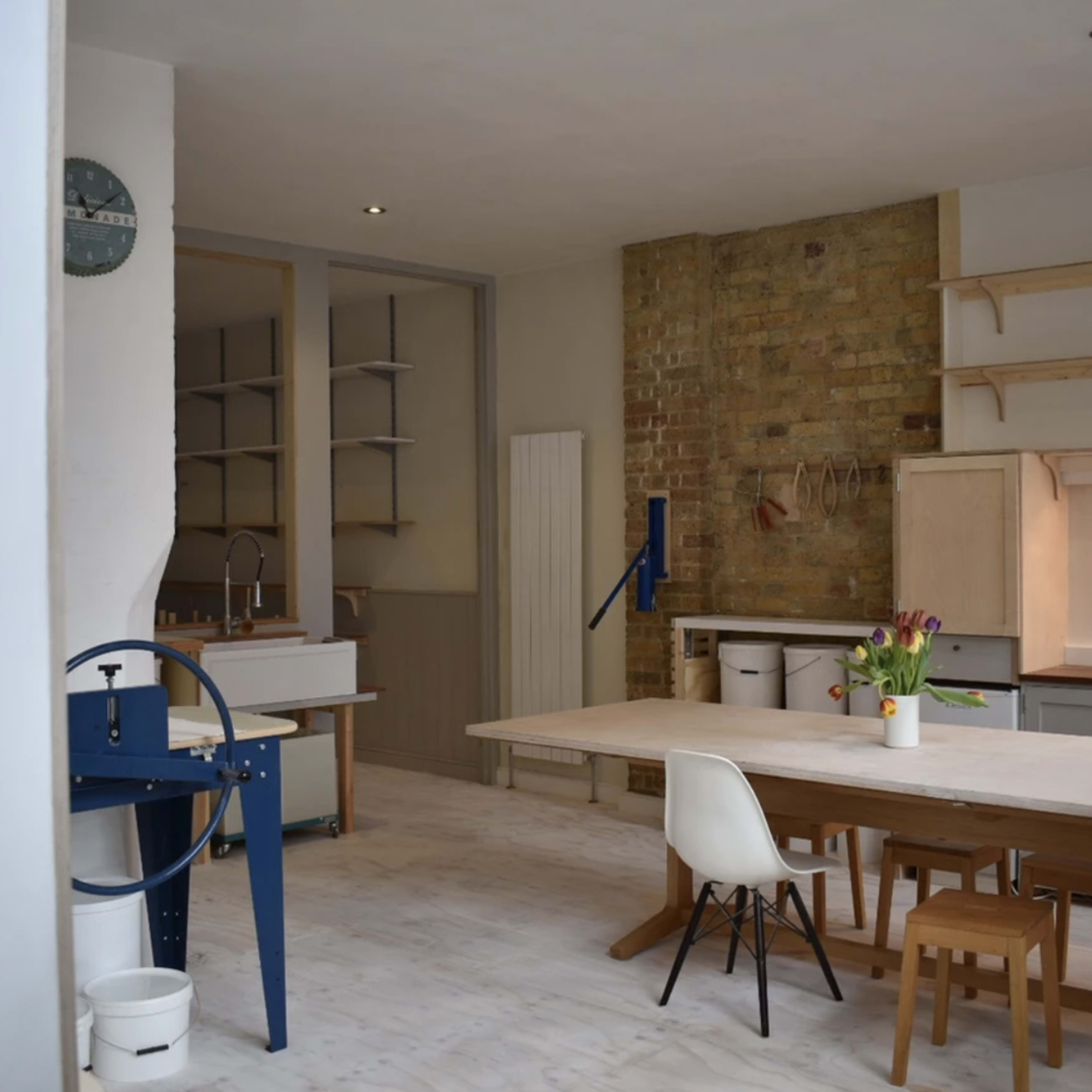 A modern, minimalistic kitchen and dining area featuring a large table, wooden chairs, and exposed brick walls.