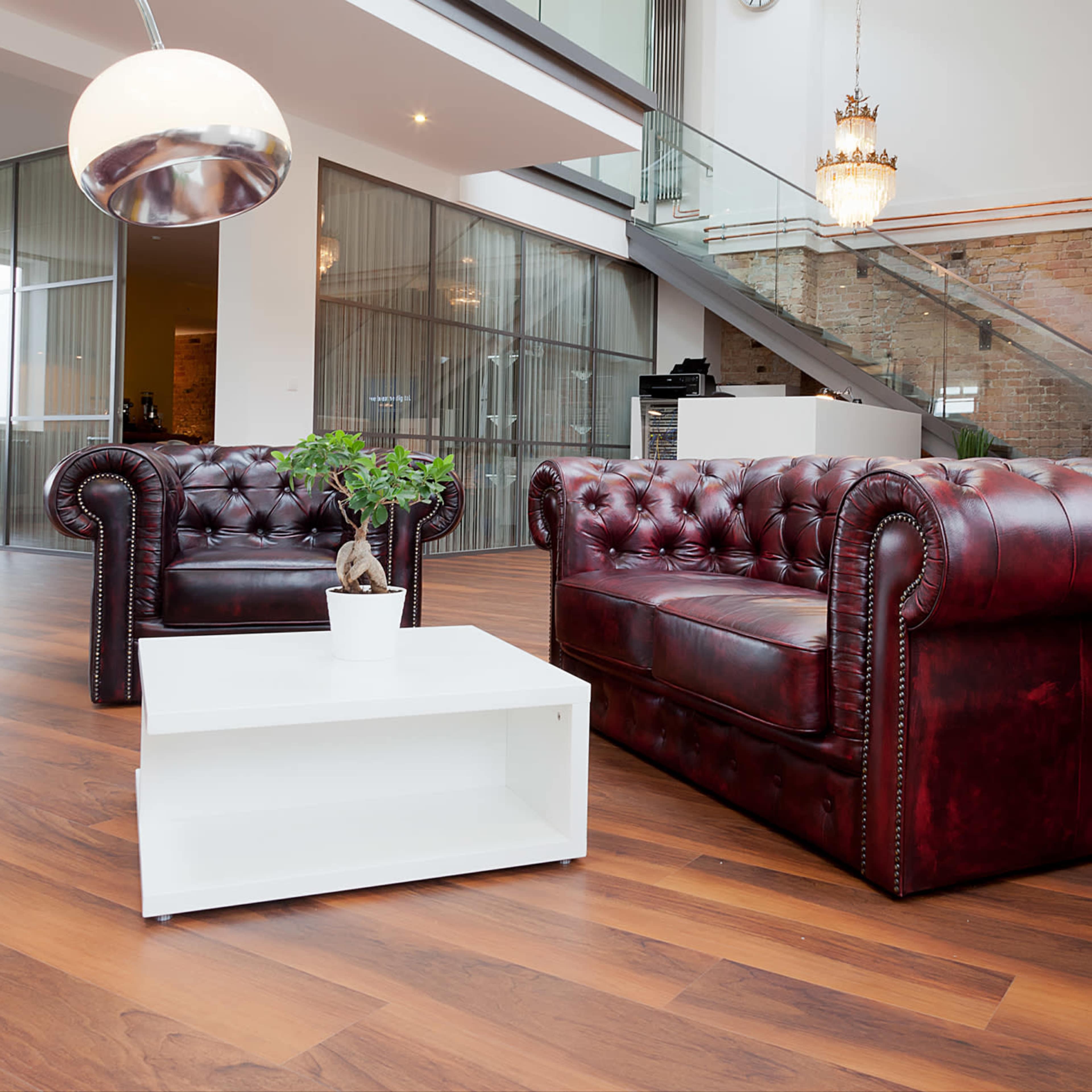 A modern, open living space with hardwood floors, featuring two burgundy leather sofas and a white coffee table.