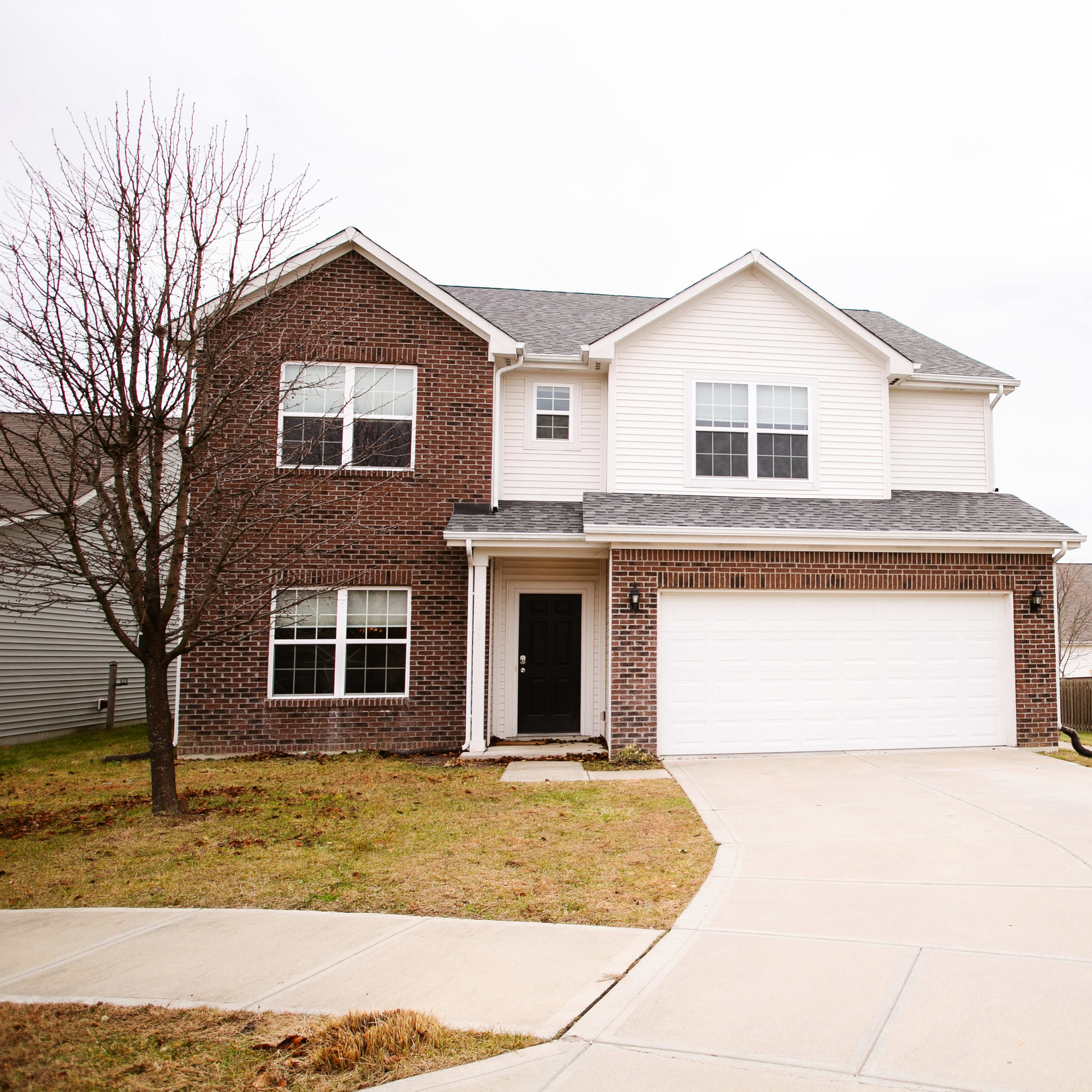 A two-story residential home with a brick facade, a large front garage, and a concrete driveway.