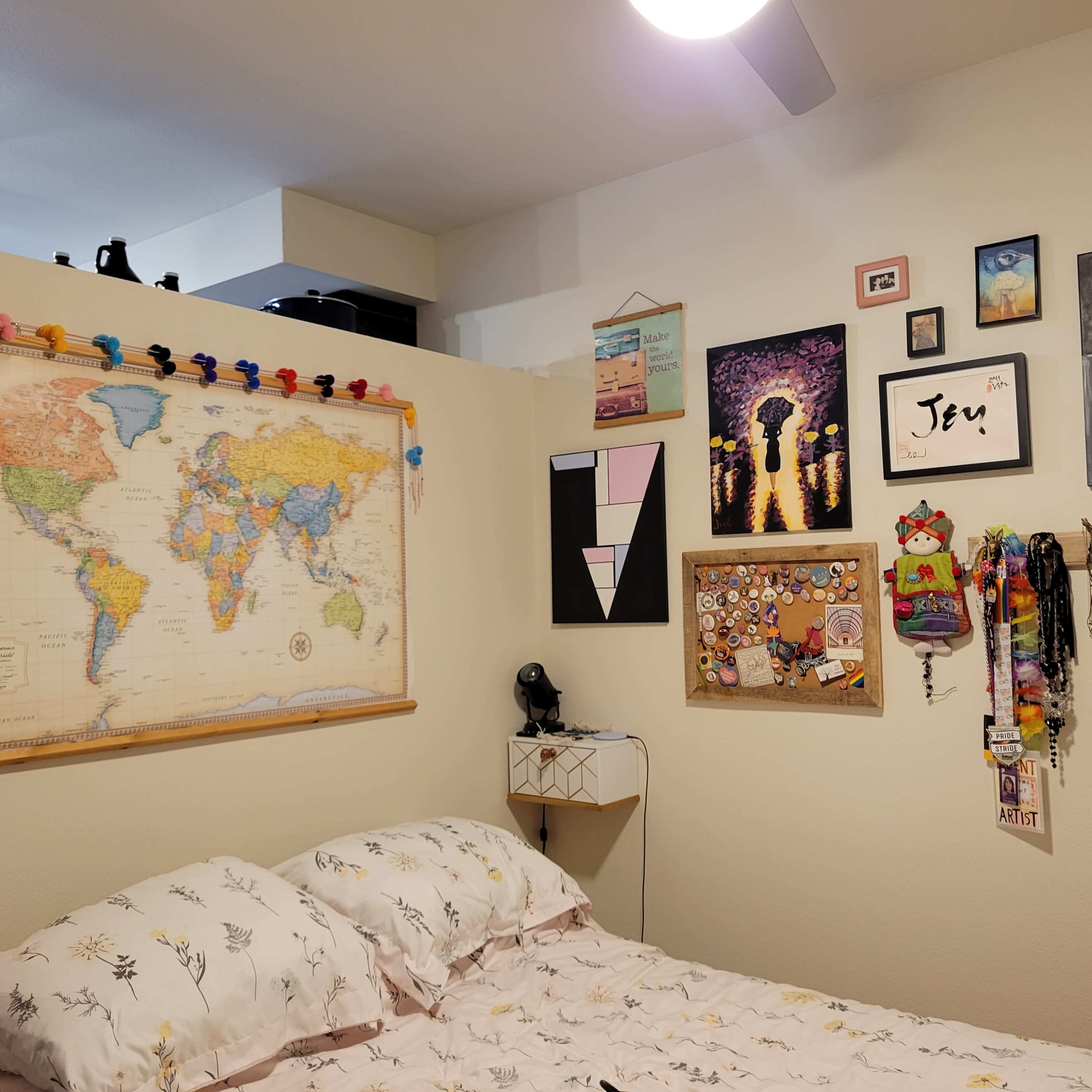 A cozy bedroom with a large world map on one wall and various framed artworks and decorations arranged around it.