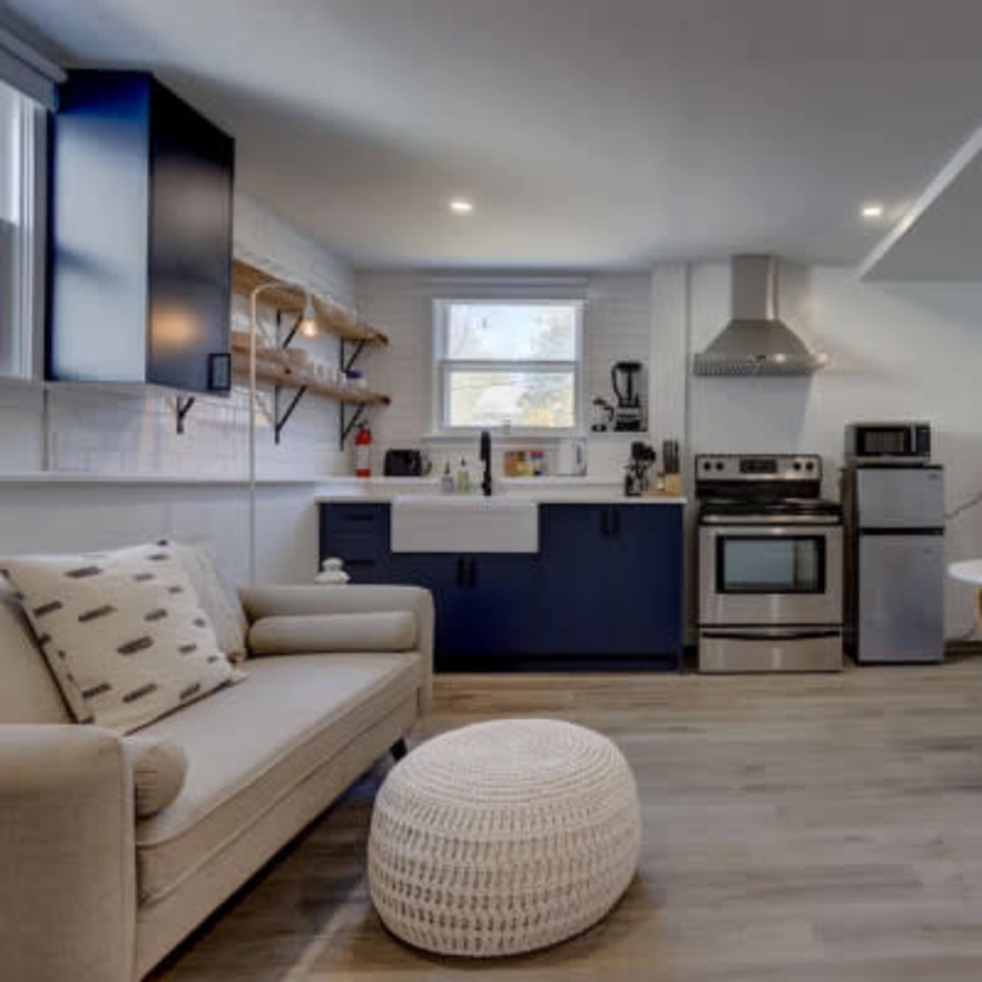 A modern kitchen features stainless steel appliances, a white sink, and a small dining table with rattan chairs.