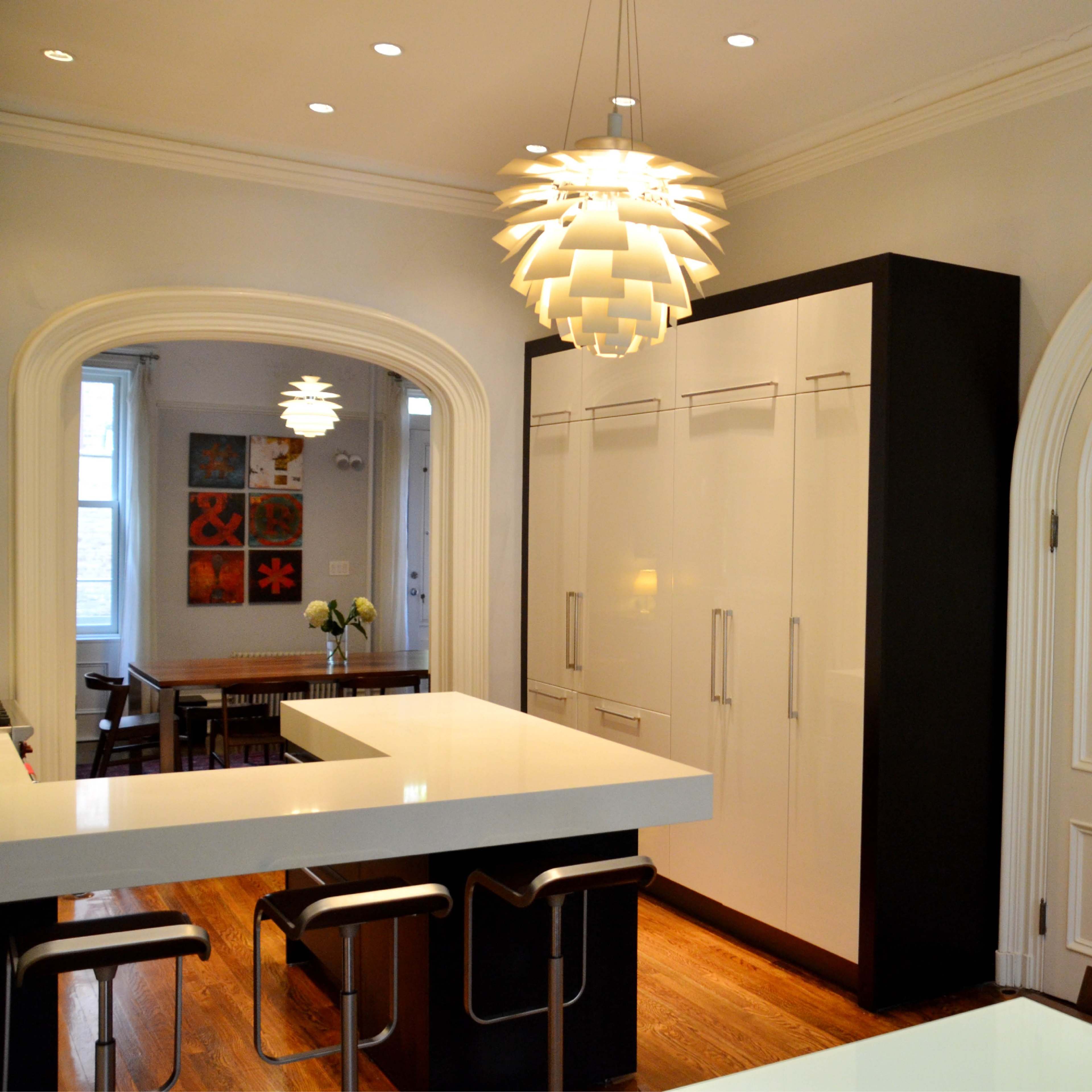 A modern kitchen with a large white island, a unique pendant light, and sleek cabinetry along one wall.