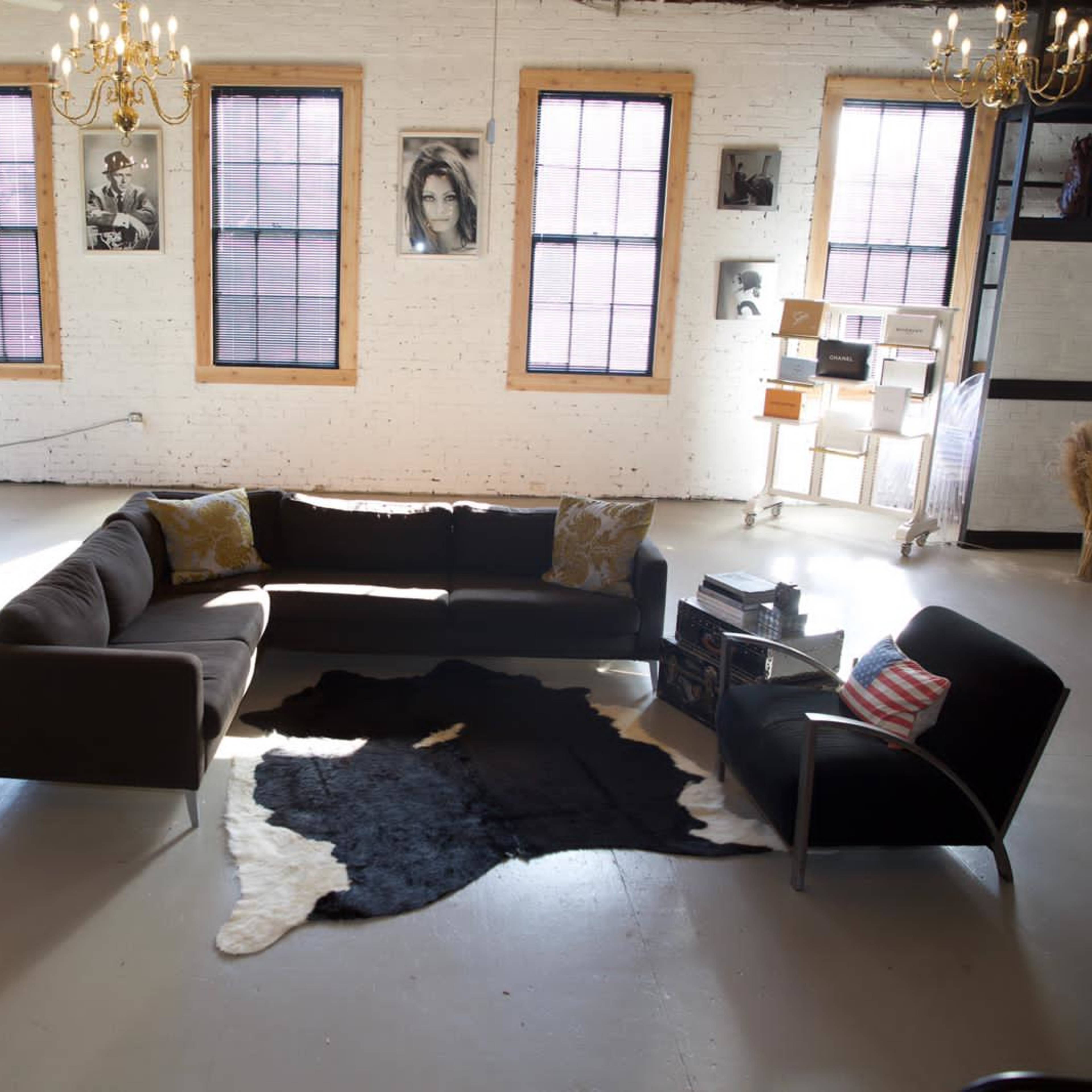 A spacious room with large windows, featuring a sectional sofa, a cowhide rug, and a dining area with clear chairs and a display shelf.