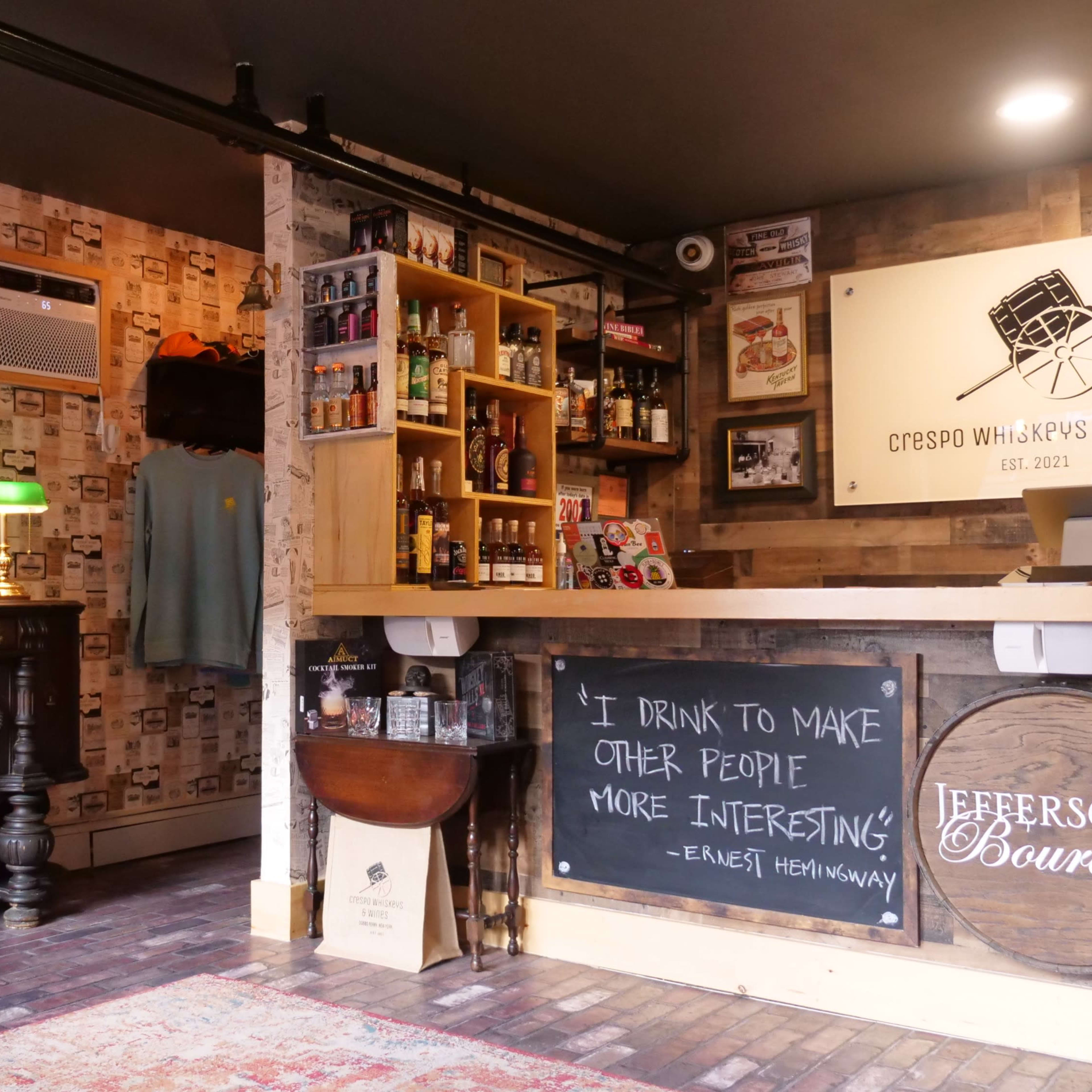 A cozy bar area featuring shelves stocked with various liquor bottles, a chalkboard with a quote, and decorative artwork on the walls.