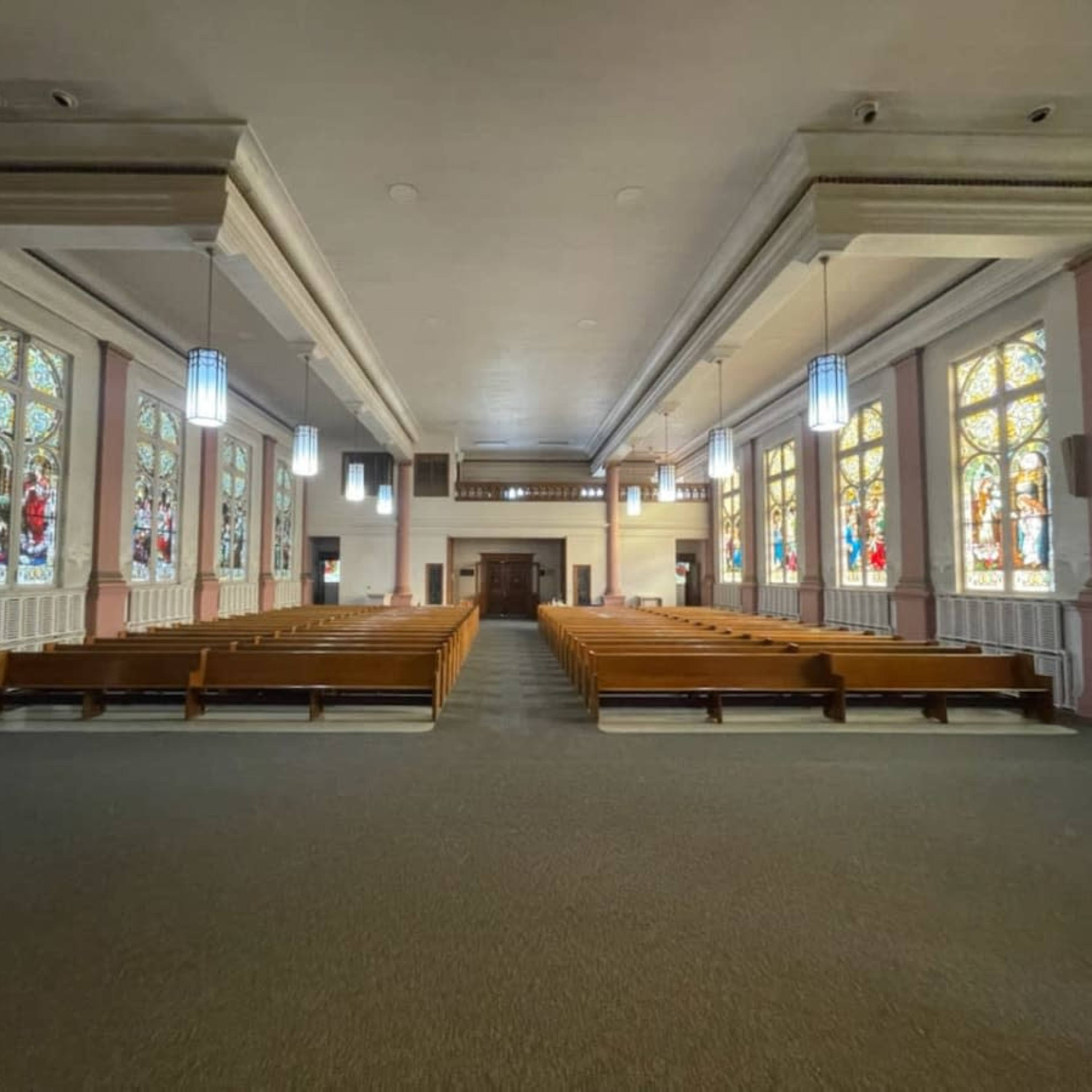 The interior of a church with wooden pews arranged in rows and colorful stained glass windows lining the walls.
