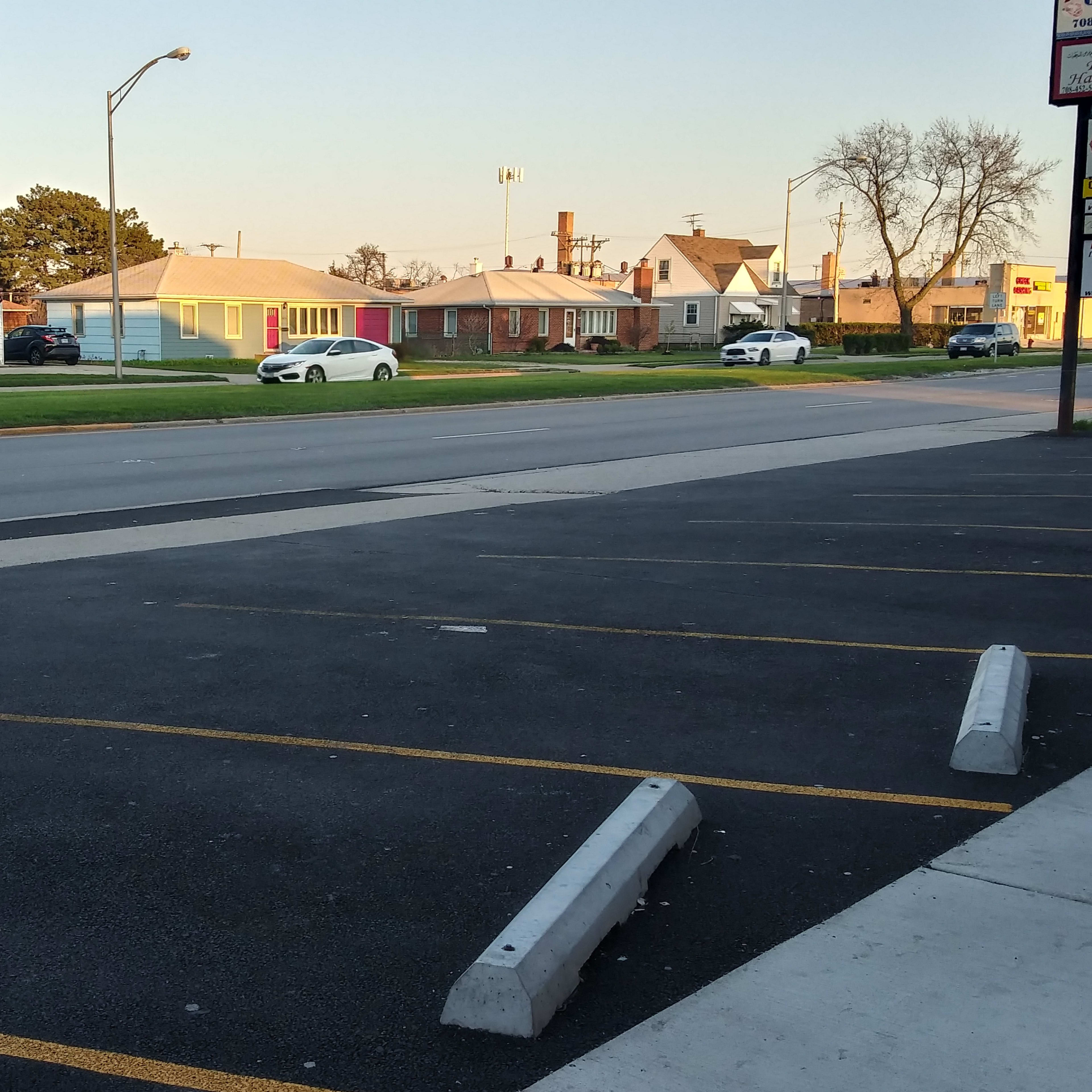 A roadside view with empty parking spaces in the foreground and a row of residential and commercial buildings across the street.