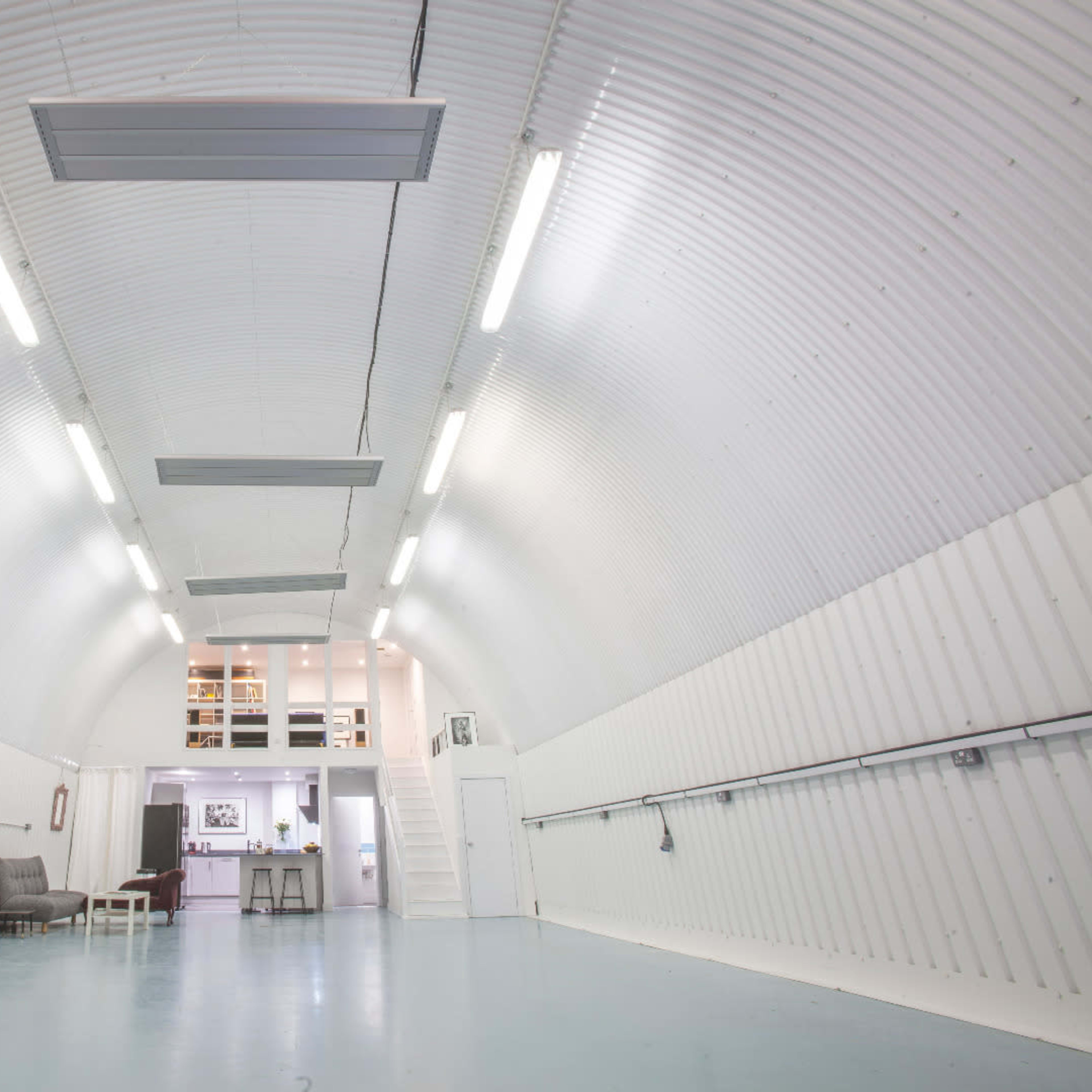 A spacious, white, corrugated interior with a high arch, featuring industrial-style lighting and a small multi-level area at the far end.
