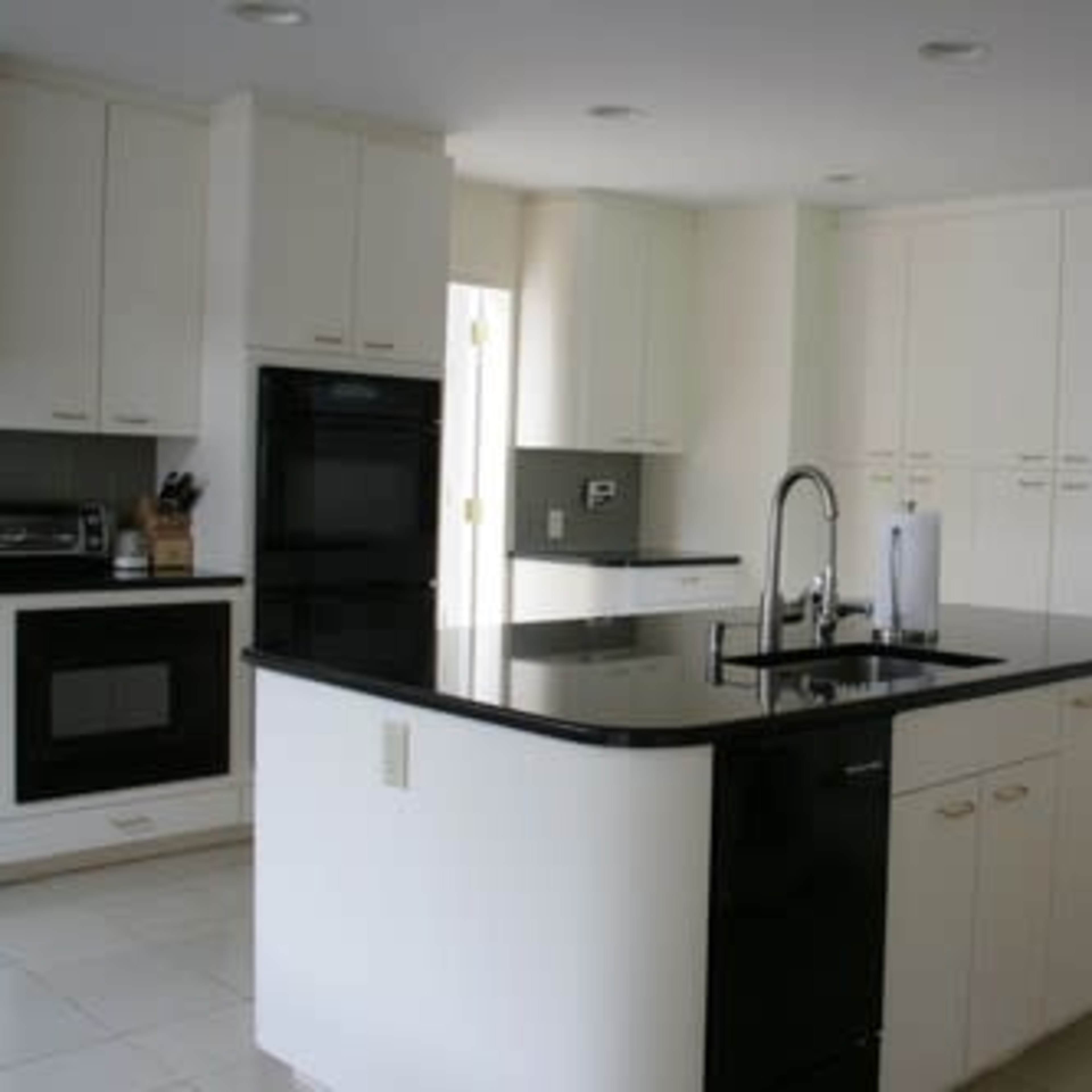 A modern kitchen featuring white cabinetry, a black countertop island, and stainless steel appliances.