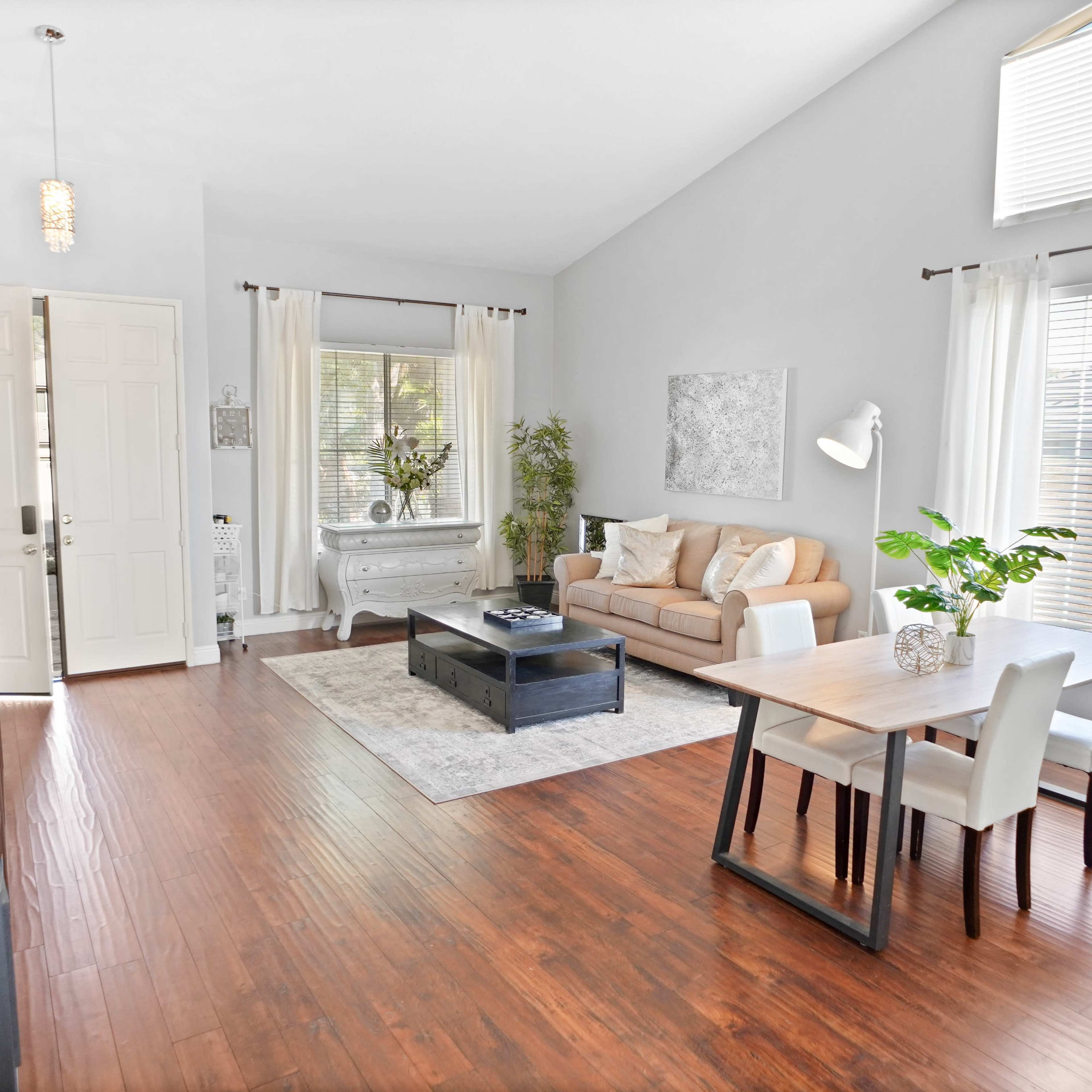 A modern living room with a sofa, a coffee table, a dining area, and large windows allowing natural light to enter.