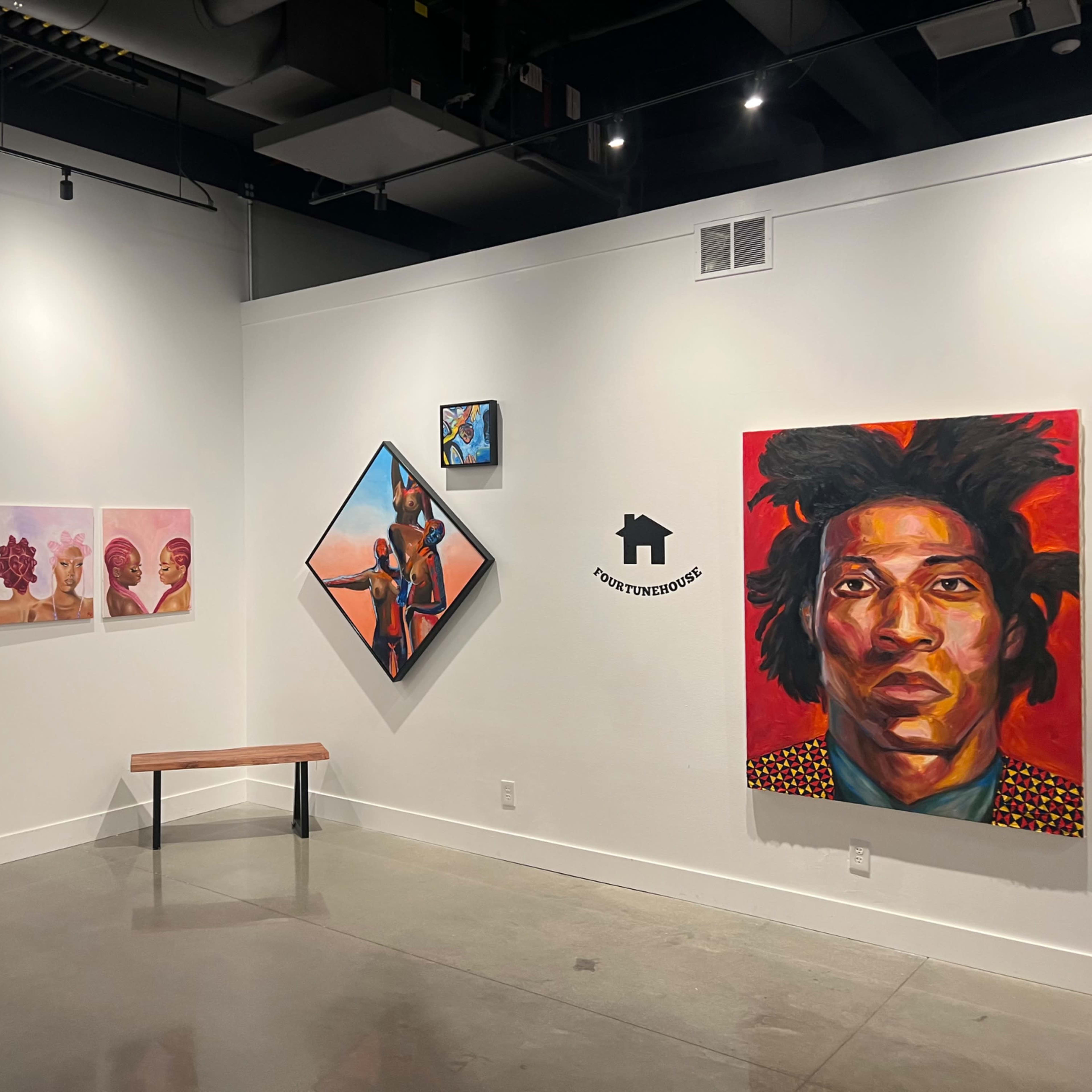 An art gallery wall displaying a variety of artwork, including portraits and abstract pieces, with a bench in front for visitors.