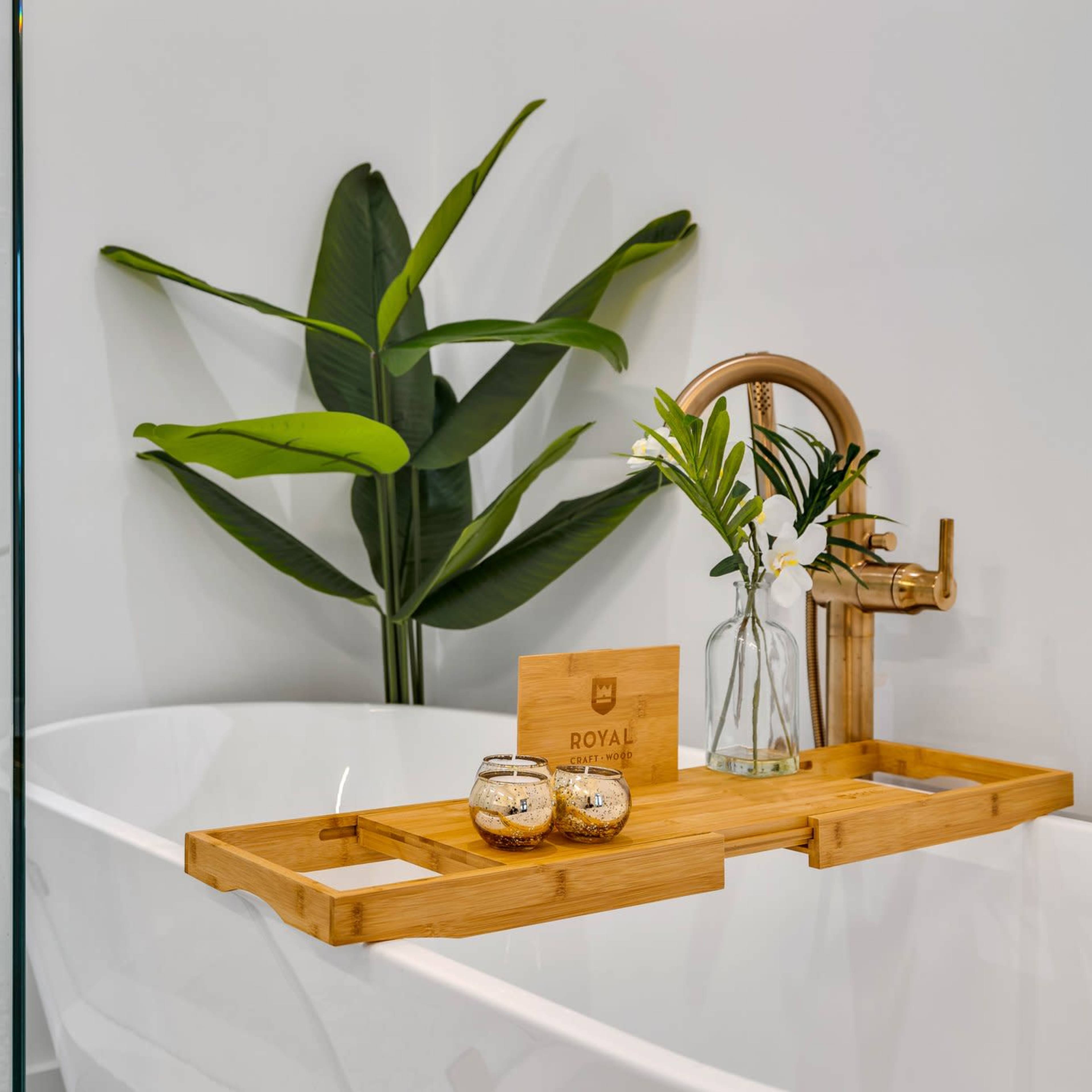 A bamboo bath tray holds decorative items and a small vase with flowers beside a freestanding bathtub and a glass shower enclosure.