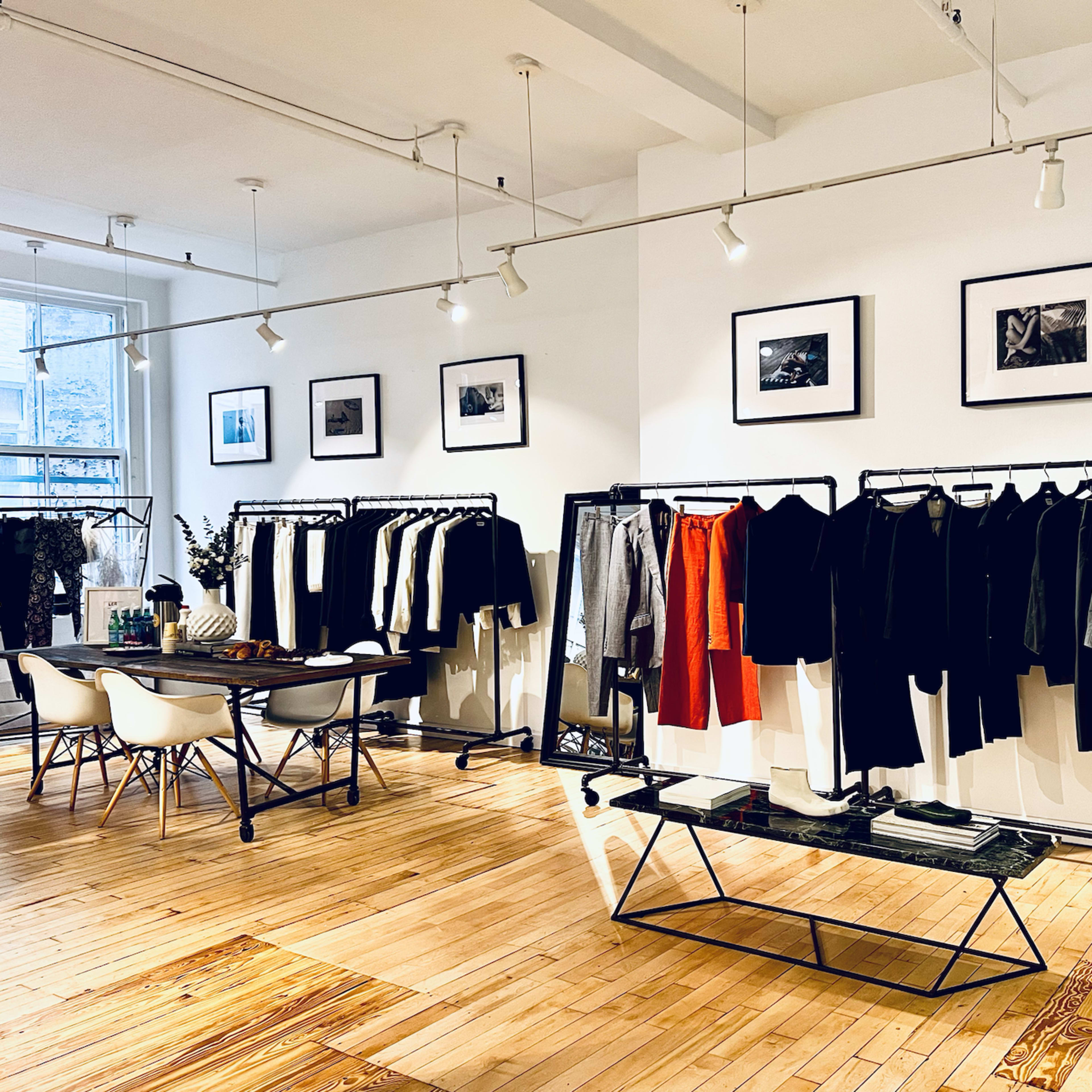 A modern showroom features racks of black and white clothing, a central table, and framed photographs on the walls.