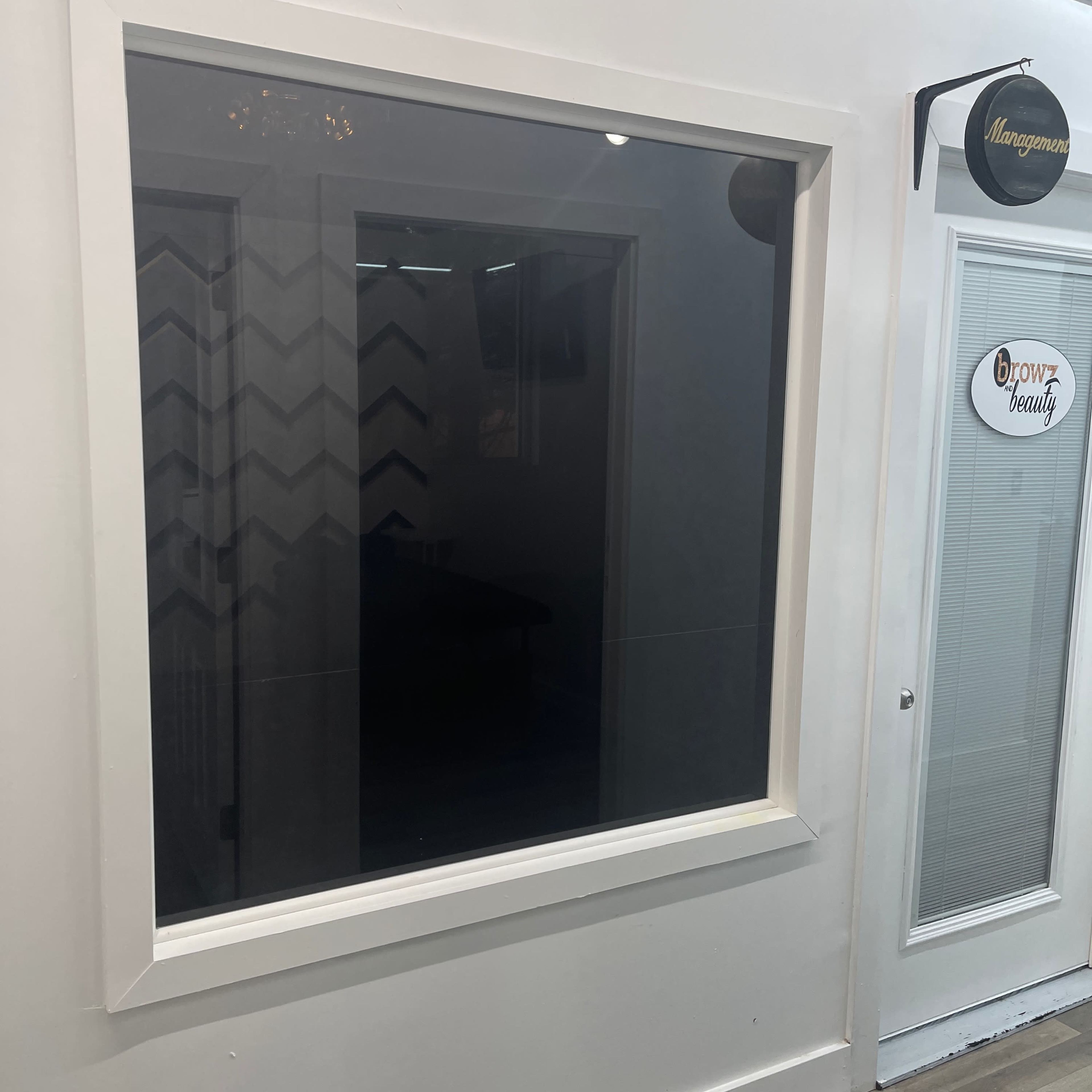 A large, blank window with a white frame is mounted on a wall next to a door labeled "Management."