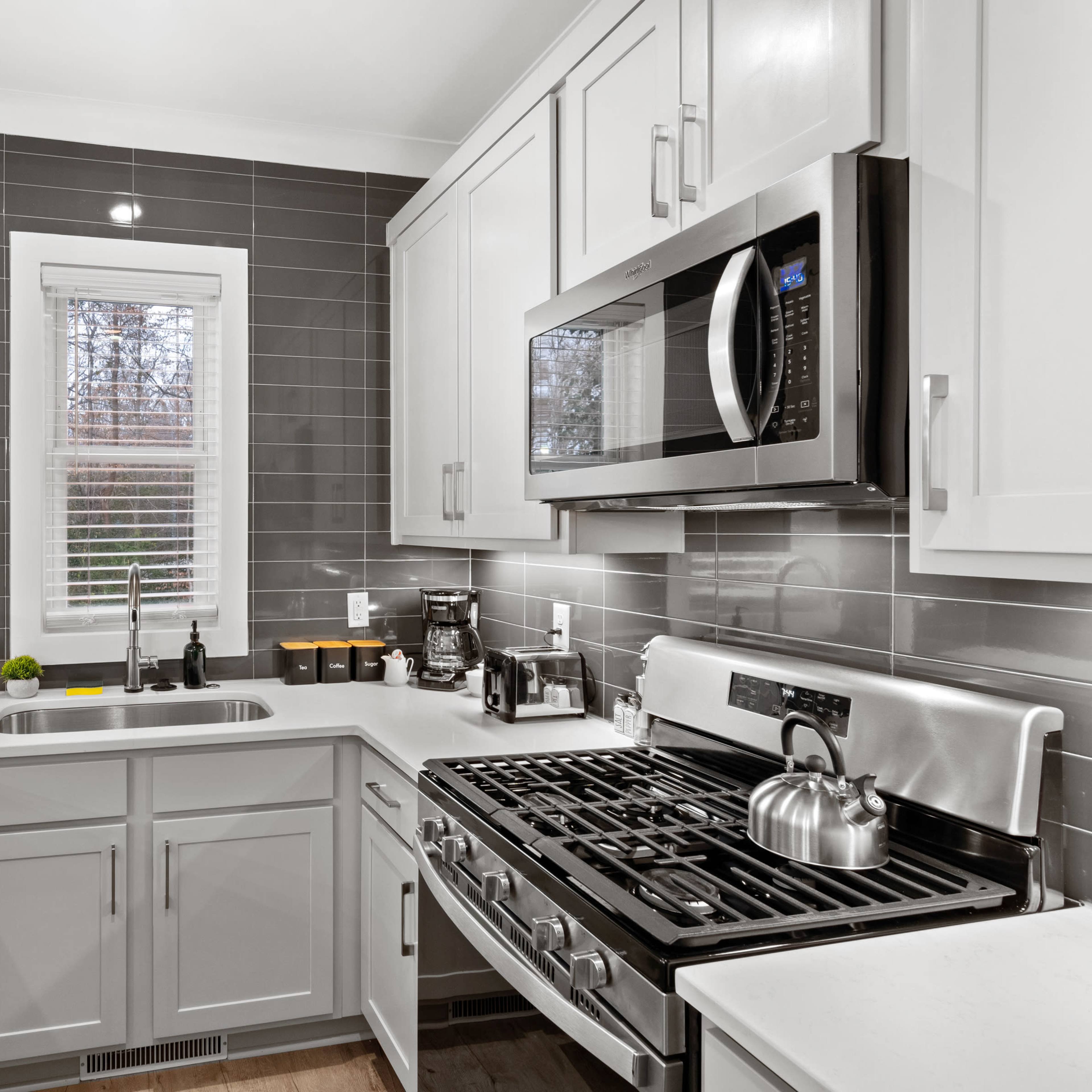 A modern kitchen with gray cabinets, stainless steel appliances, a gas stove, and a window letting in natural light.