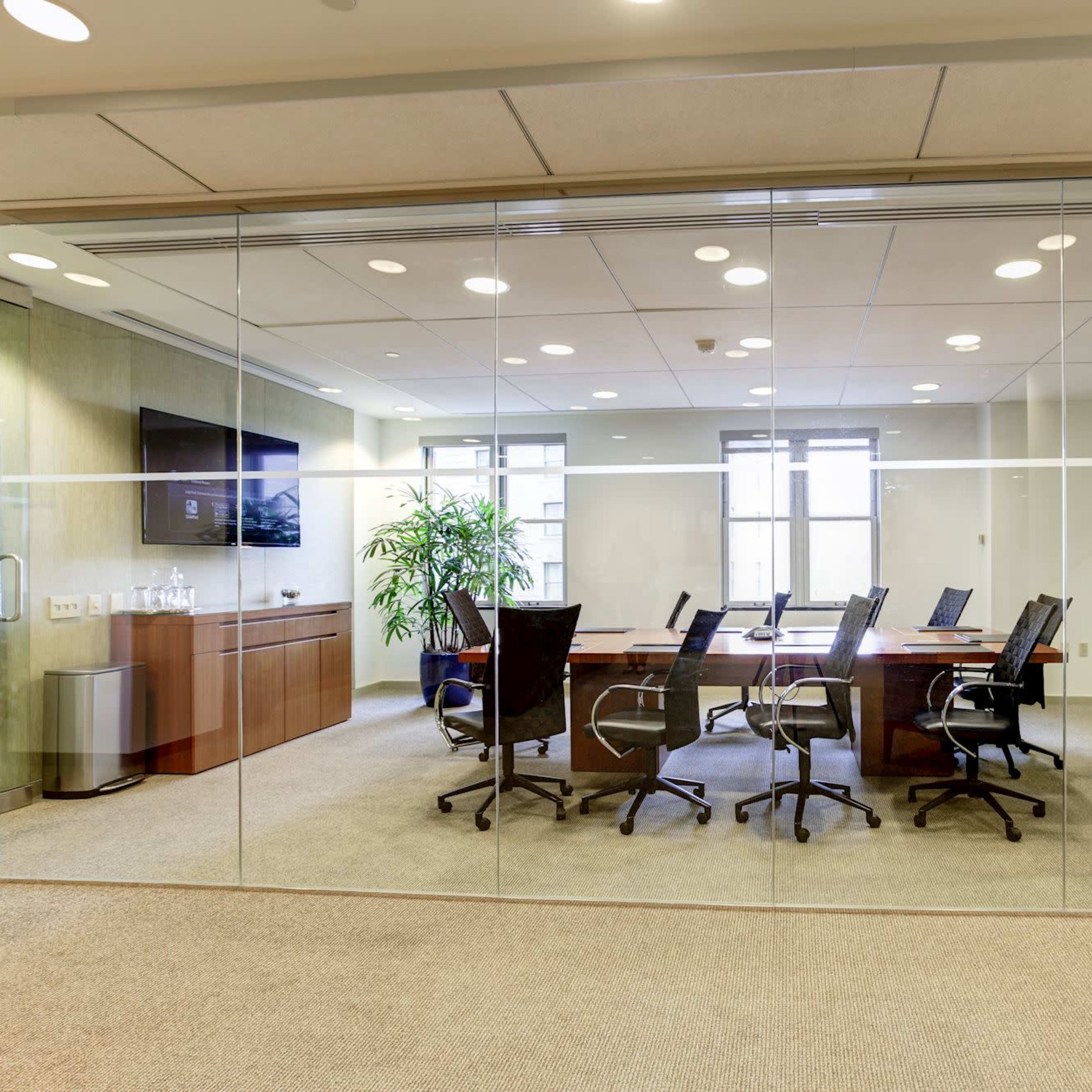 A glass-walled conference room features a large table surrounded by ergonomic chairs and potted plants.