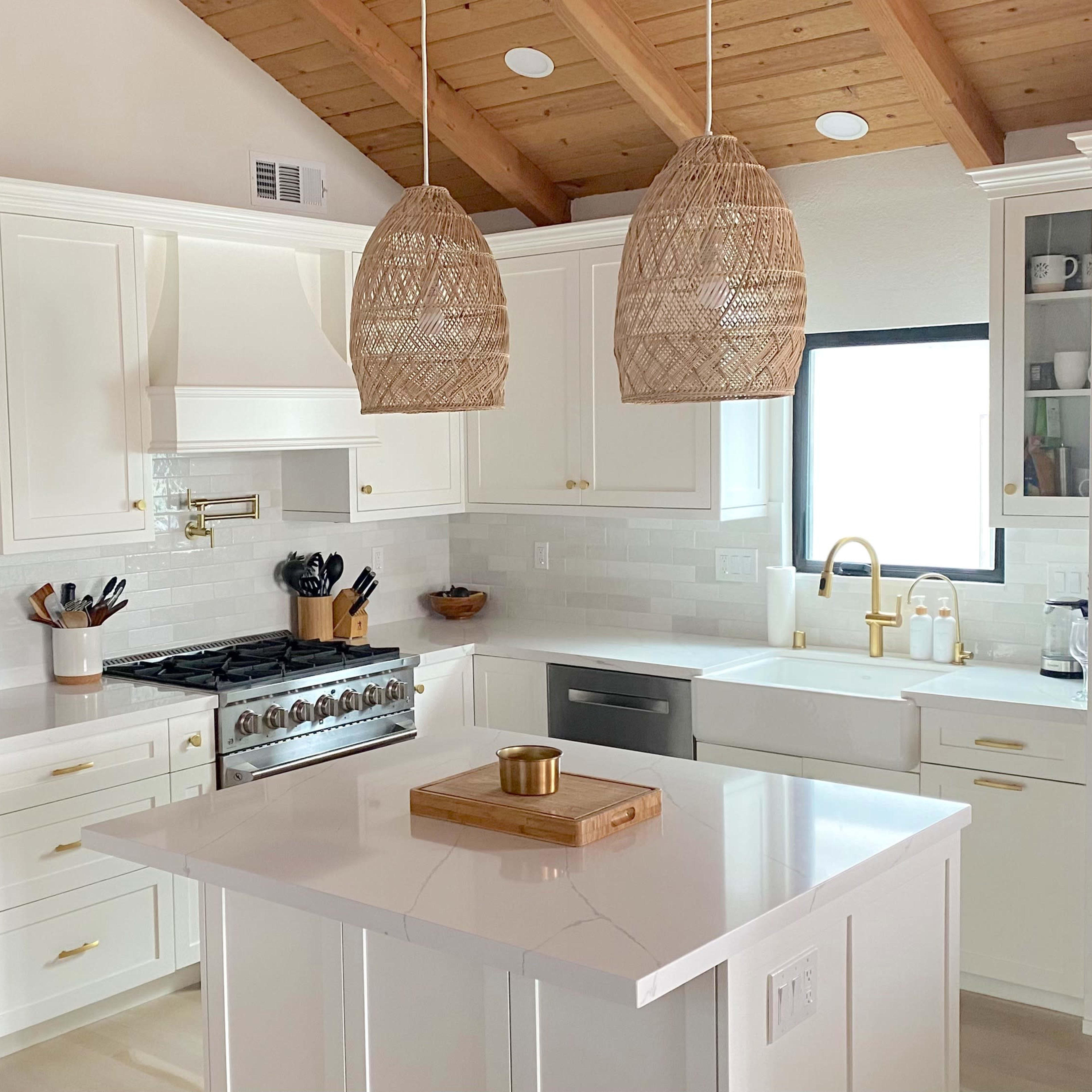 The kitchen features white cabinetry, a large island with a wooden tray, and pendant lights hanging above, complementing stainless steel appliances.