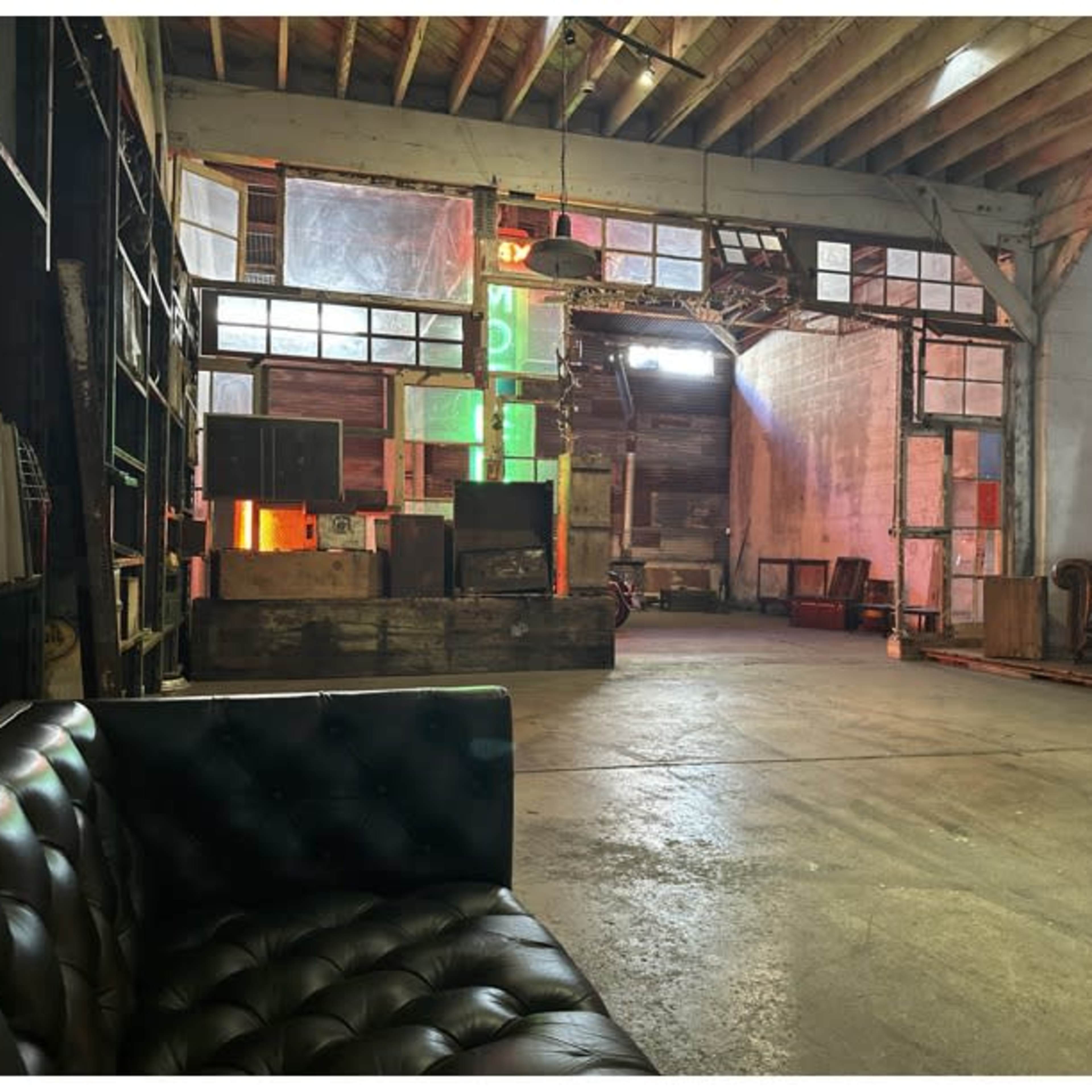 A spacious, industrial-style room with exposed wooden beams, various wooden crates, and a large sofa positioned against the wall.