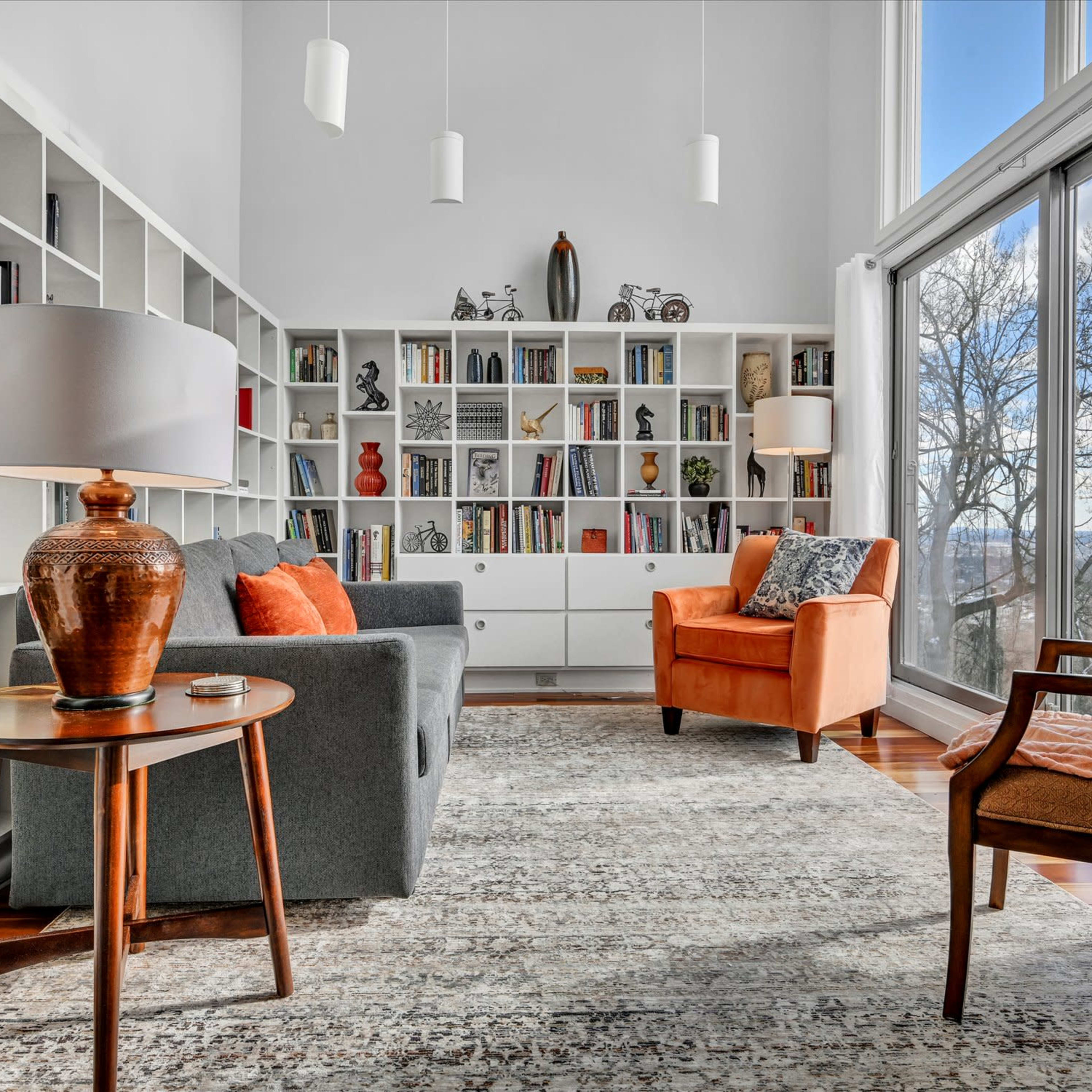 A modern living room featuring a gray sofa, an orange armchair, a round wooden side table, and a bookshelf filled with various books and decorative items.