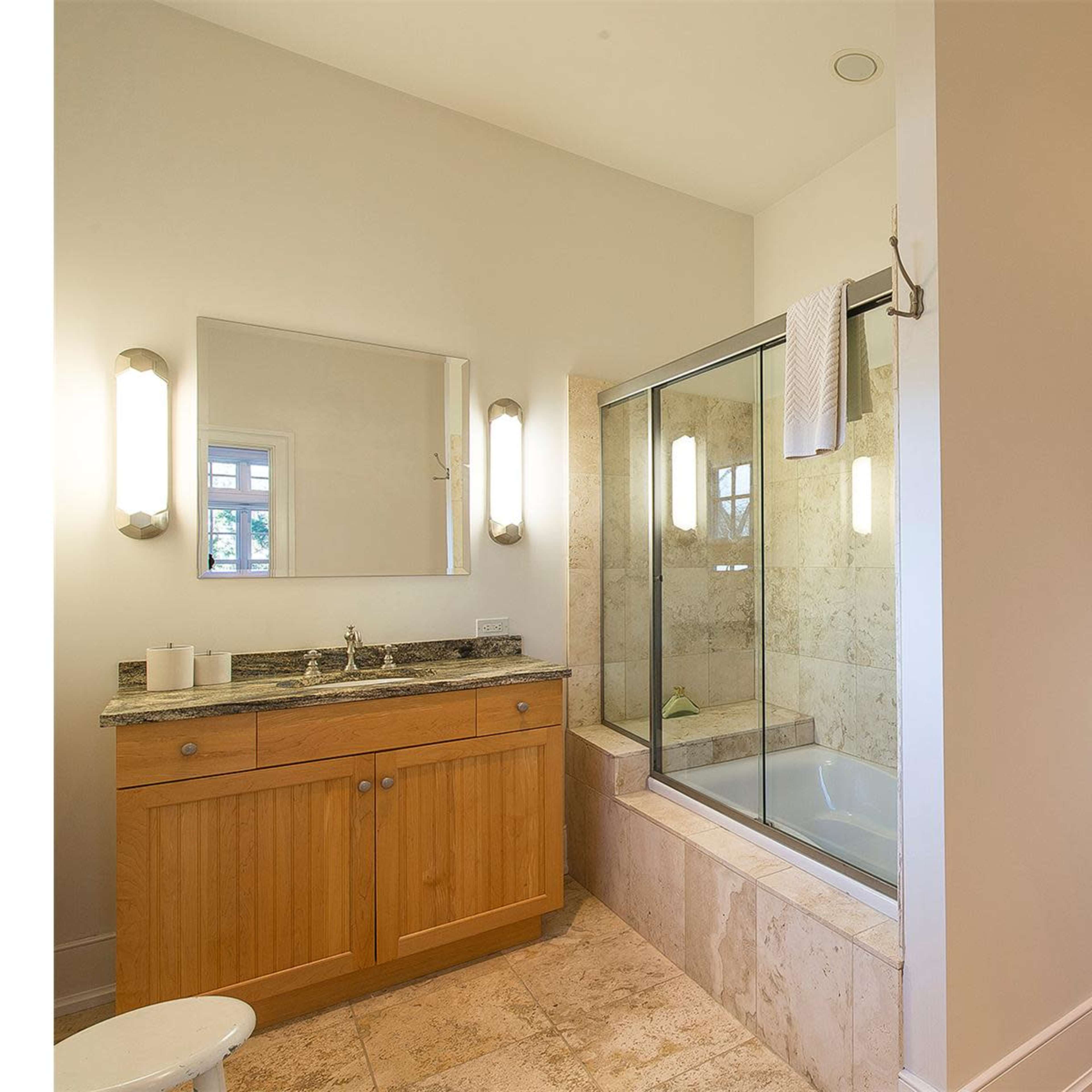 A modern bathroom with a wooden vanity, a glass shower enclosure, a bathtub, and a painting of people in a boat on the wall.