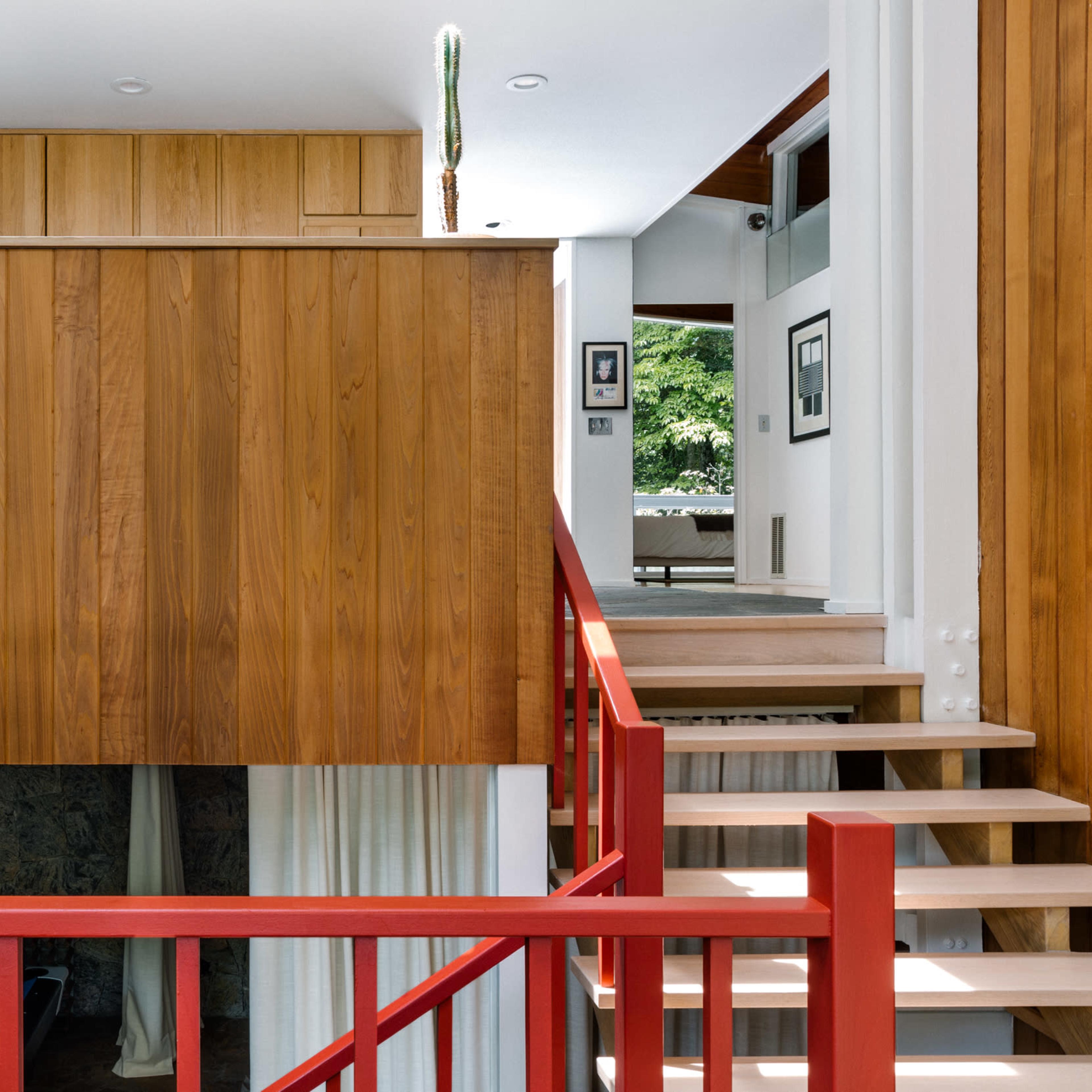 A wooden-paneled interior with a staircase, red railing, and an open living space in a contemporary home.