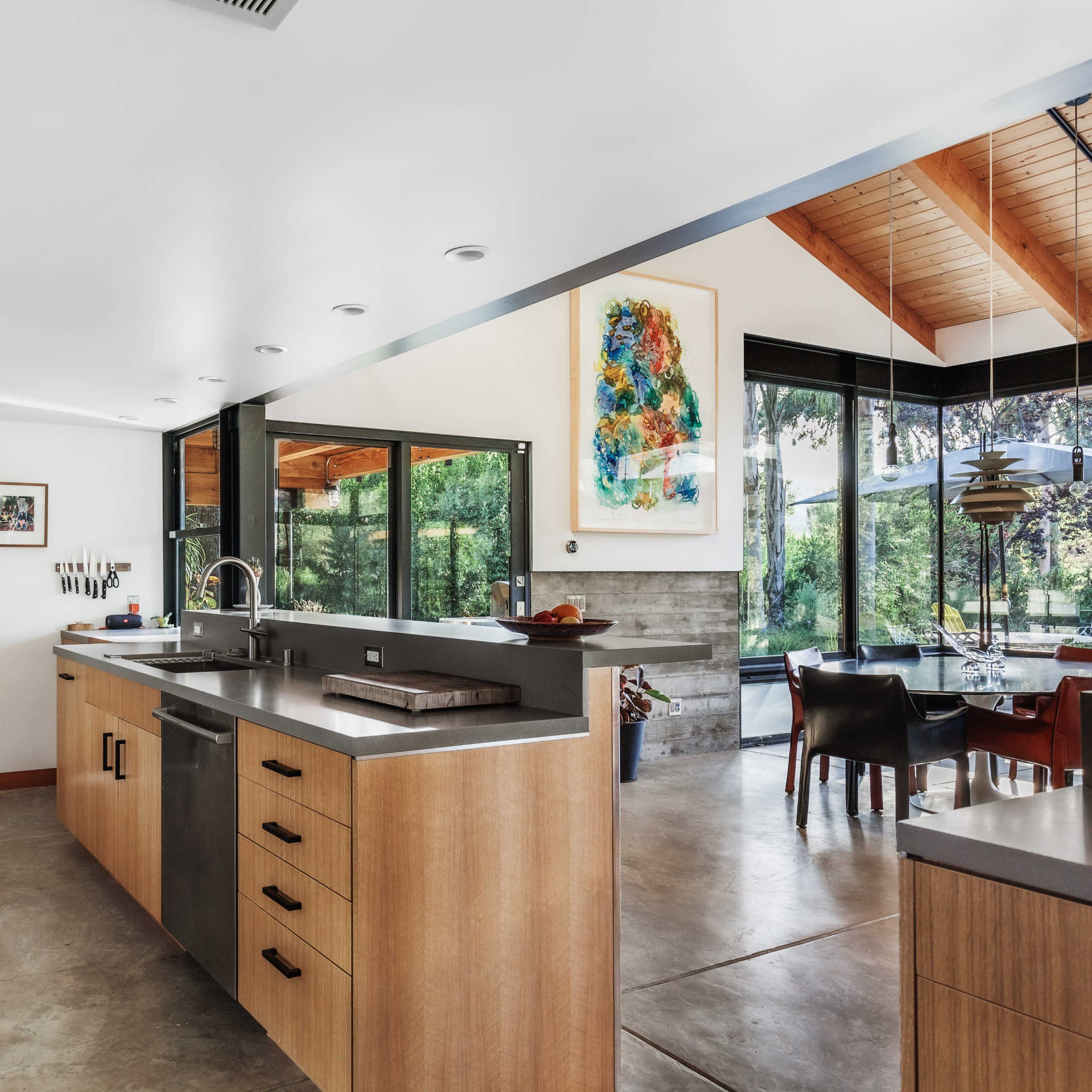 A modern kitchen with wooden cabinetry, stainless steel appliances, and large windows overlooking a garden.