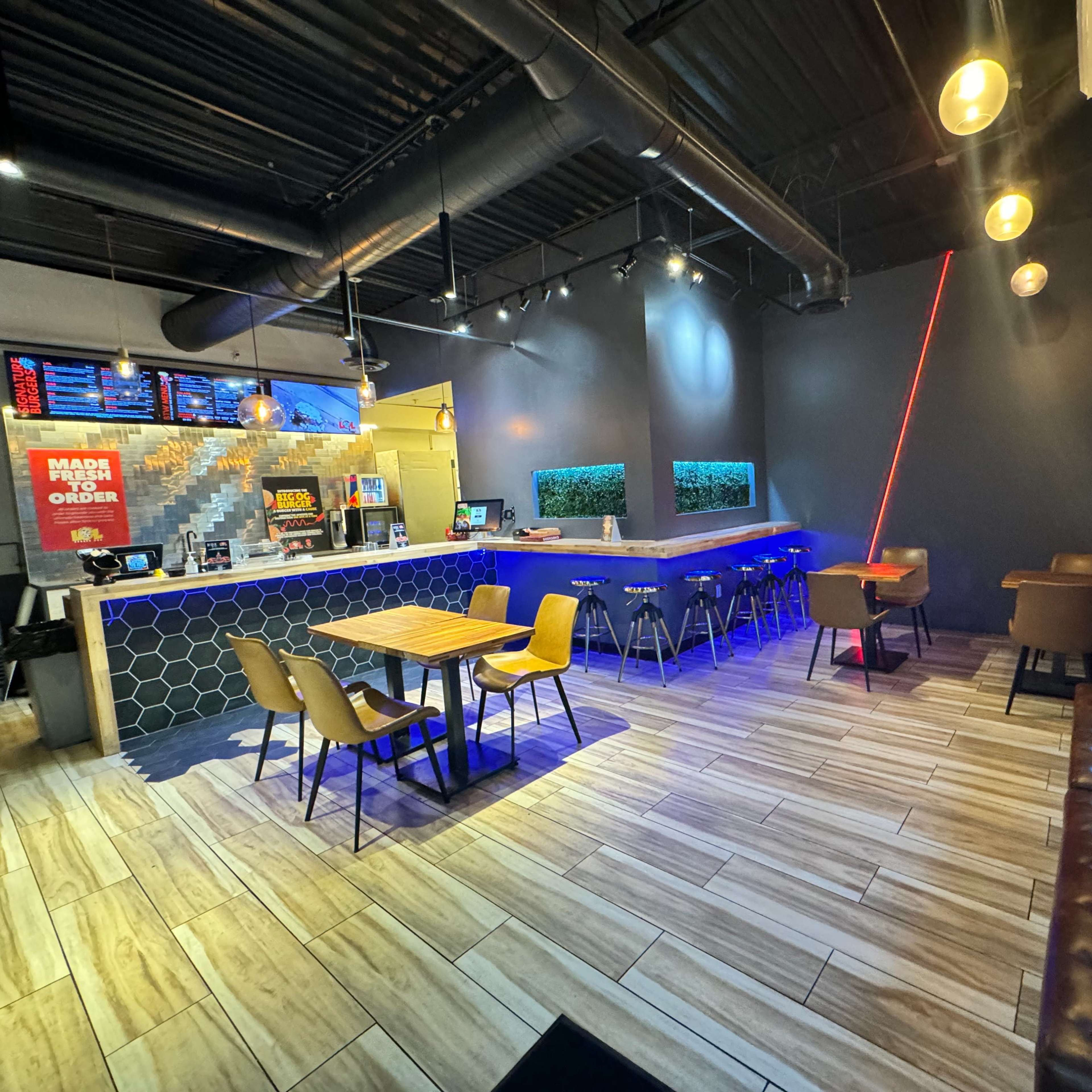 A modern restaurant interior featuring a bar area, wooden tables, and a seating space with a leather bench.