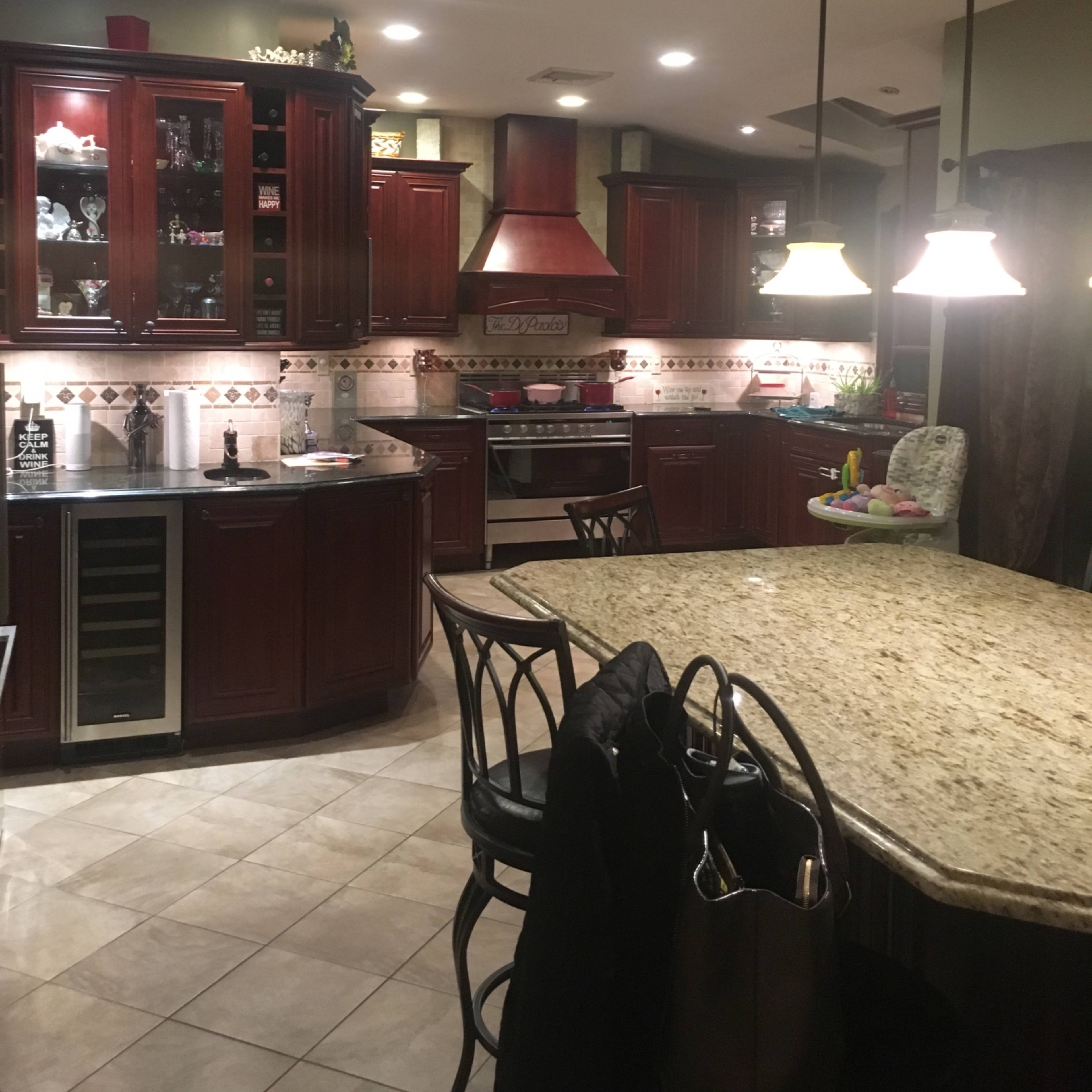 A spacious kitchen features dark wooden cabinetry, granite countertops, and an island with bar stools, illuminated by pendant lights.