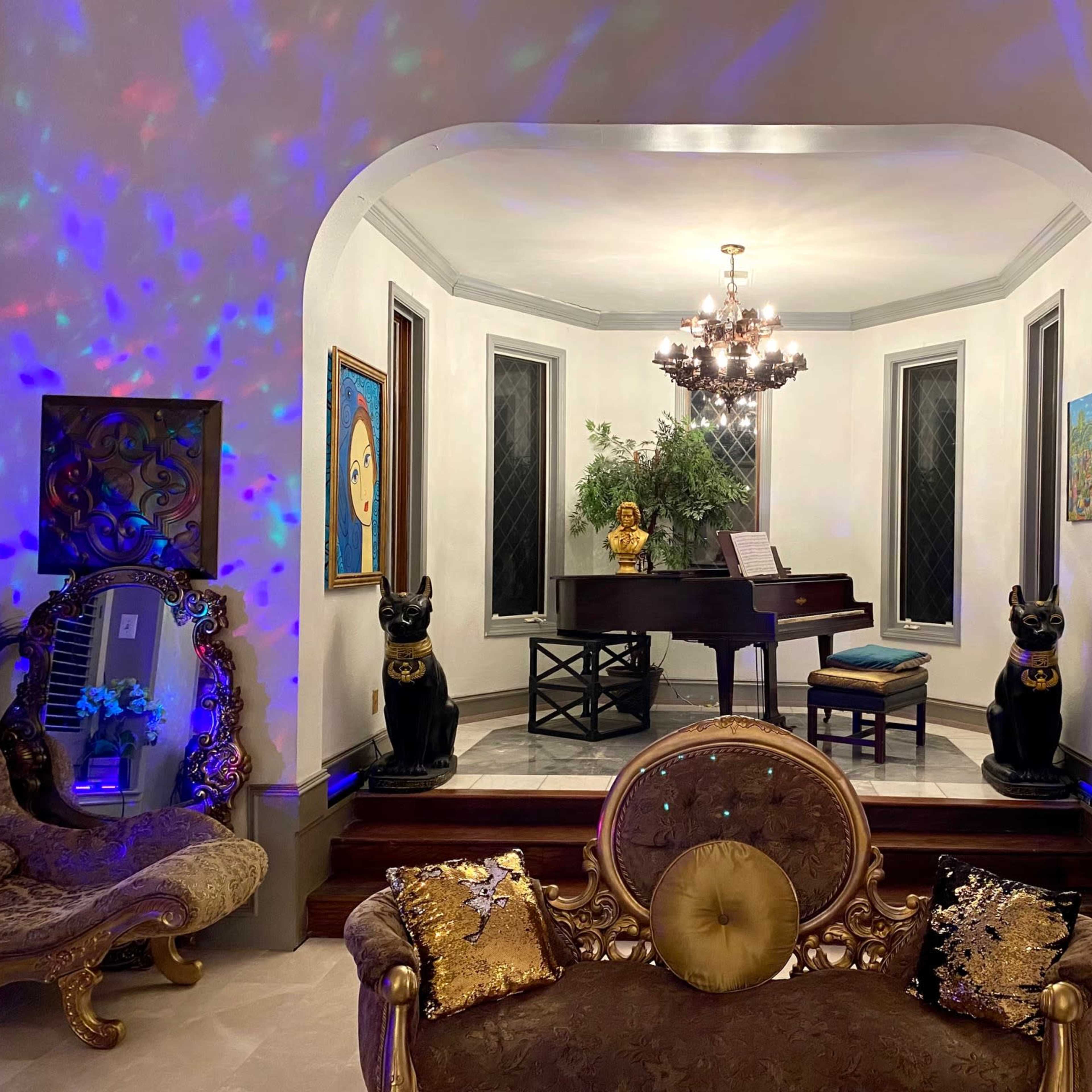An elegantly decorated room featuring a grand piano at its center, flanked by two large cat statues and adorned with various pieces of art on the walls.