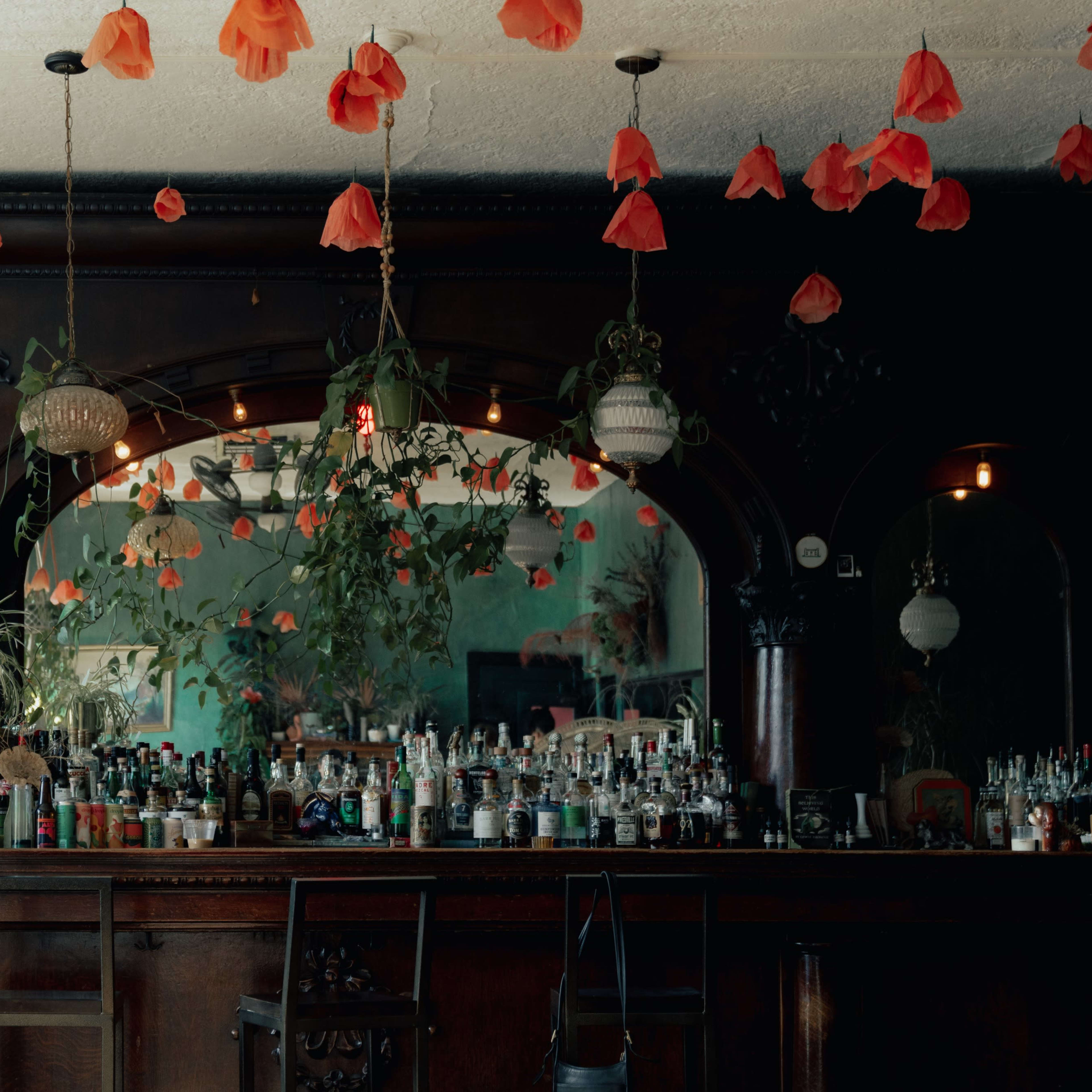 A bar interior decorated with hanging red flower petals and surrounded by dark wooden elements and plants.