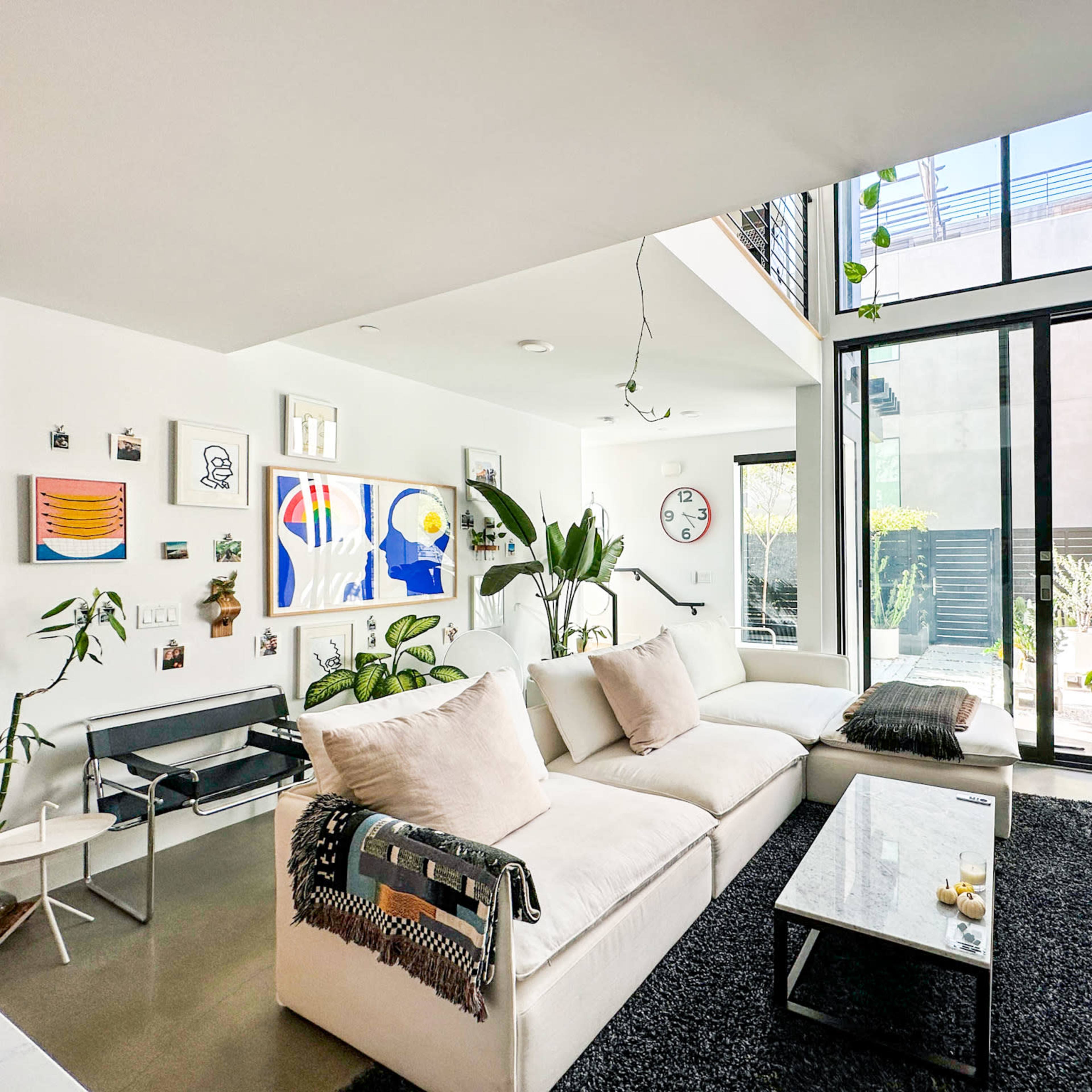A modern living room with large windows, a sectional sofa, a coffee table, plants, and art on the walls.