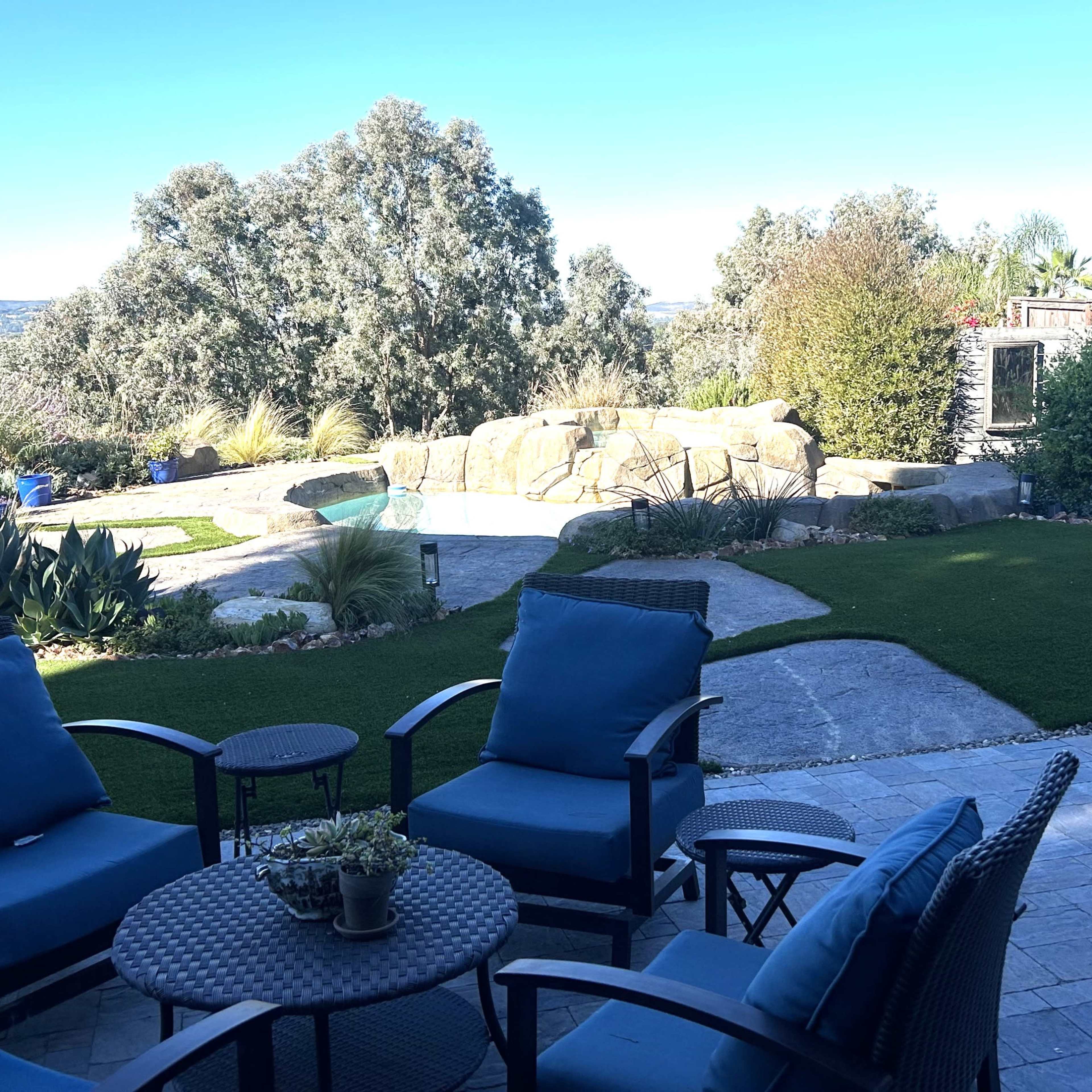 A well-maintained backyard with stone pathways, a water feature, and seating arranged around a small table.